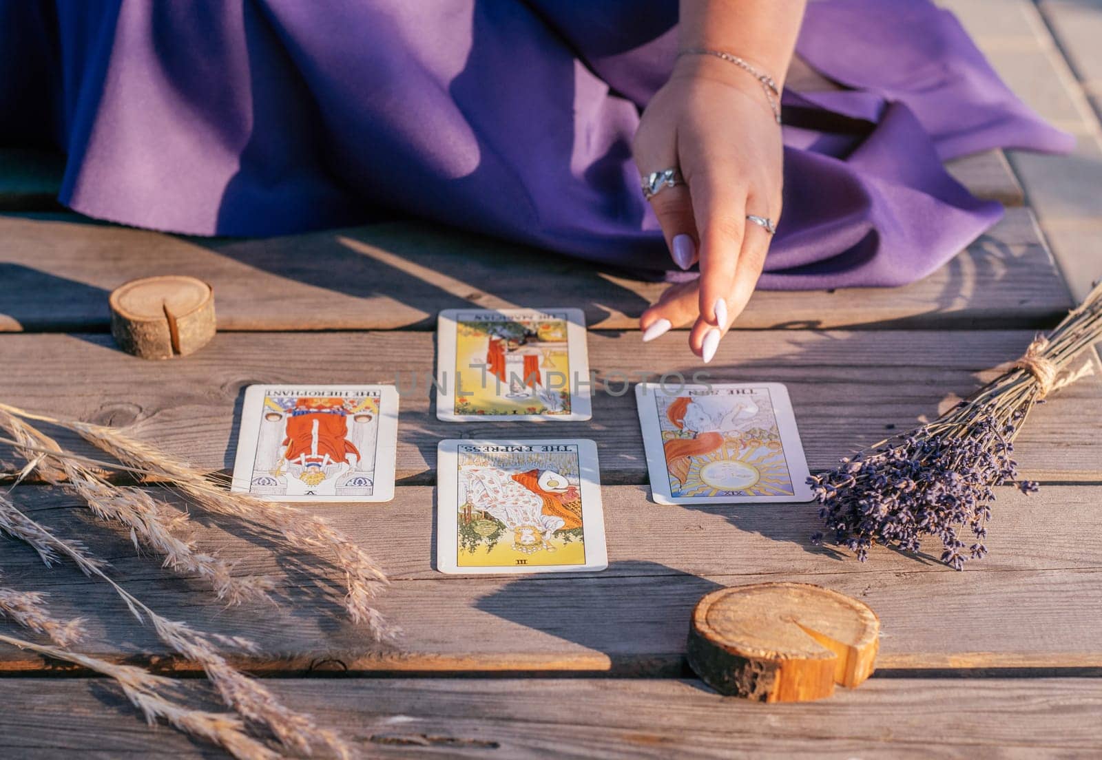 Woman's hand with purple nails points to four Tarot cards spread out on wooden surface next to spikelets and lavender. Minsk, Belarus - 07.28.2021