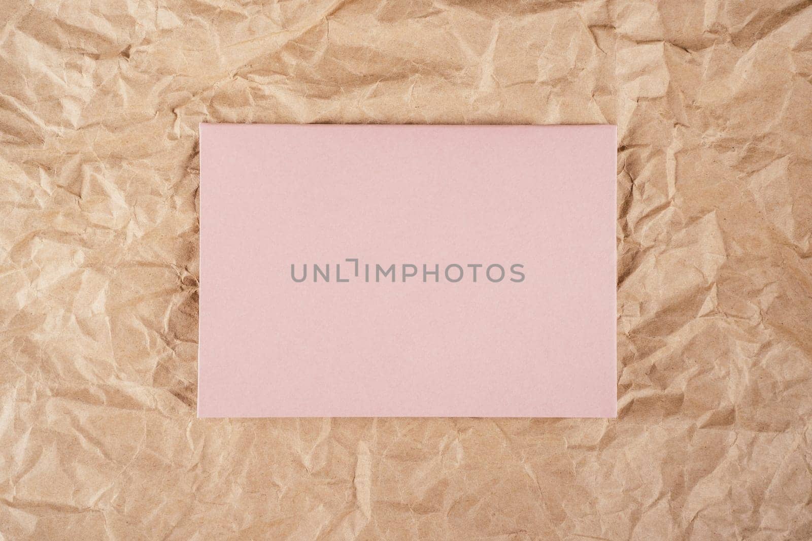 Background image of rough crumpled recycled textured kraft paper with sheet of pale pink cardboard in middle. Top view. Copy space