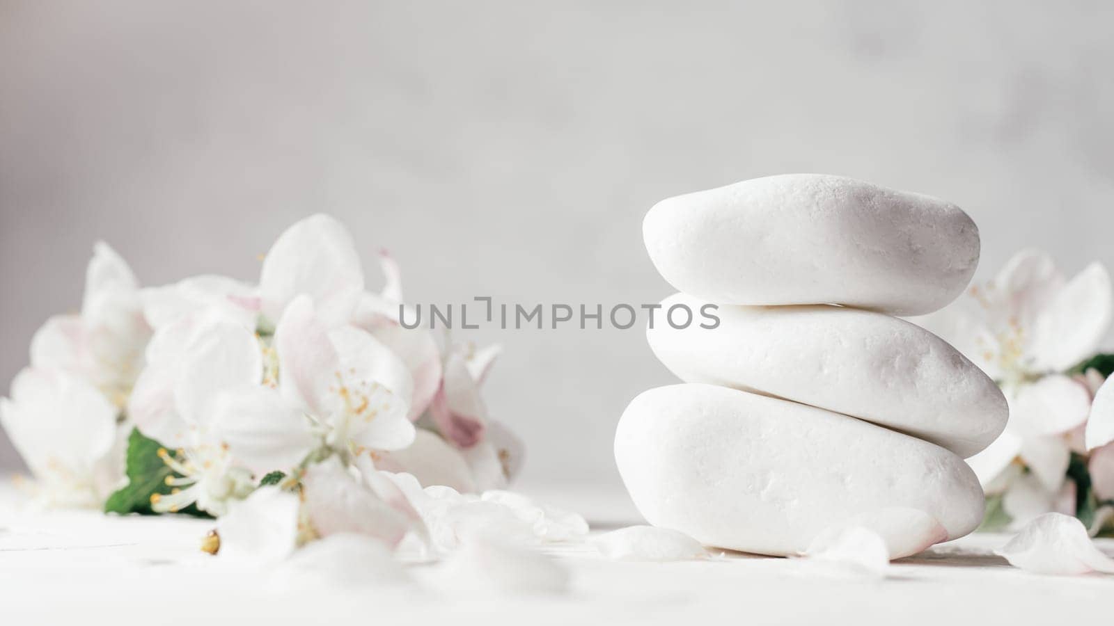 Stack of white pebble stones on light plaster surface with apple flowers. Banner