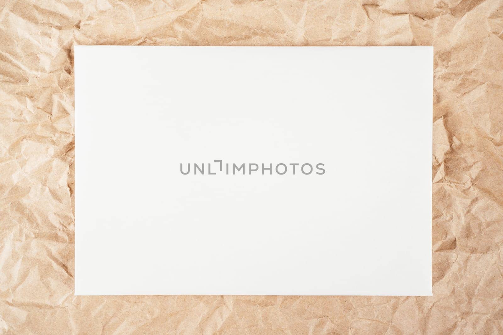 Background image of rough crumpled recycled textured kraft paper with sheet of white cardboard in middle. Top view. Copy space