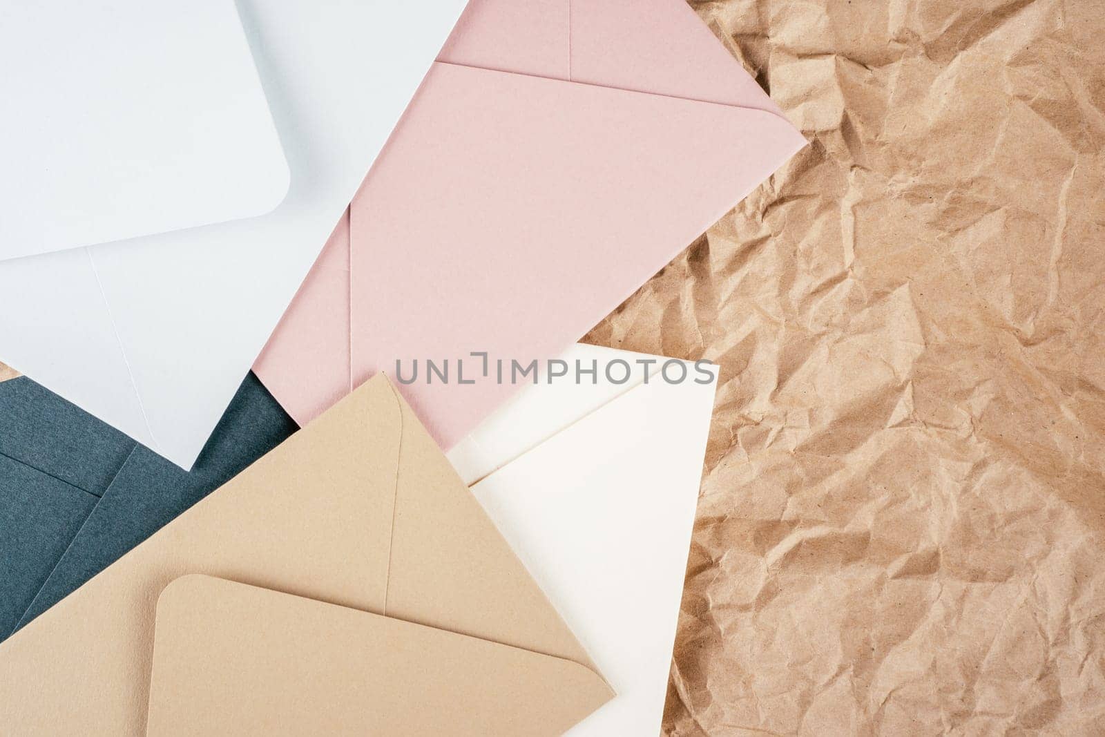 Background image of rough crumpled recycled textured kraft paper with multi-colored cardboard envelopes. Top view. Copy space