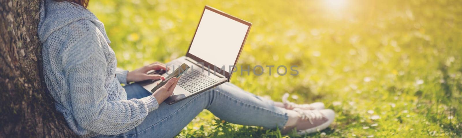 Woman with laptop sitting on the grass in the natural park. Concept of the freelance, working and learning.