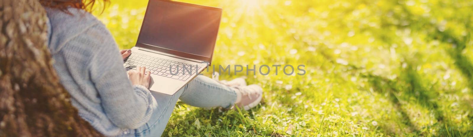 Woman with laptop sitting on the grass in the natural park. Concept of the freelance, working and learning.
