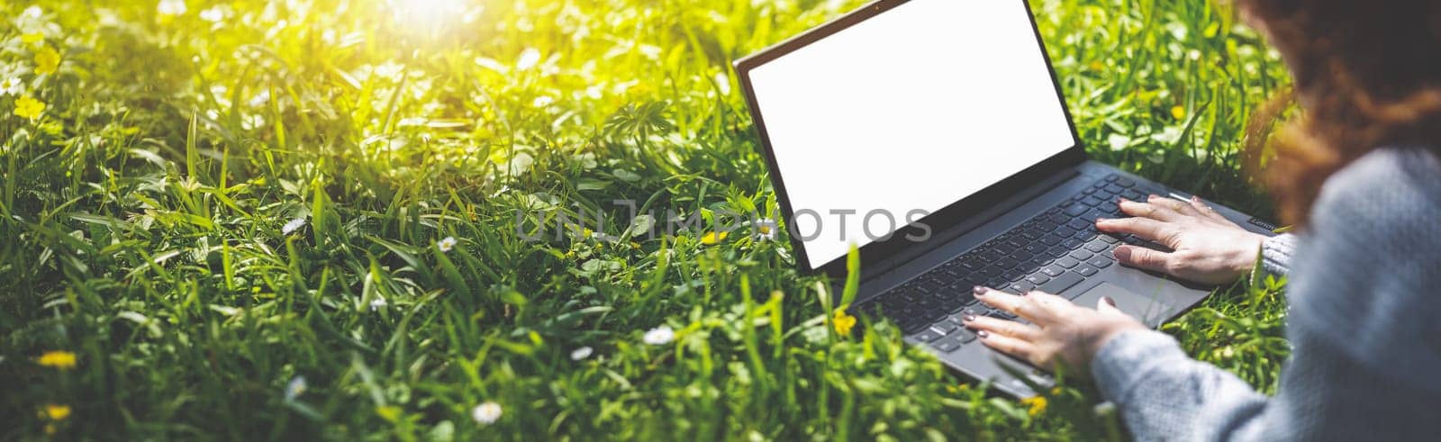 Woman lying with laptop on the blossoming meadow in natural park. Panoramic background.