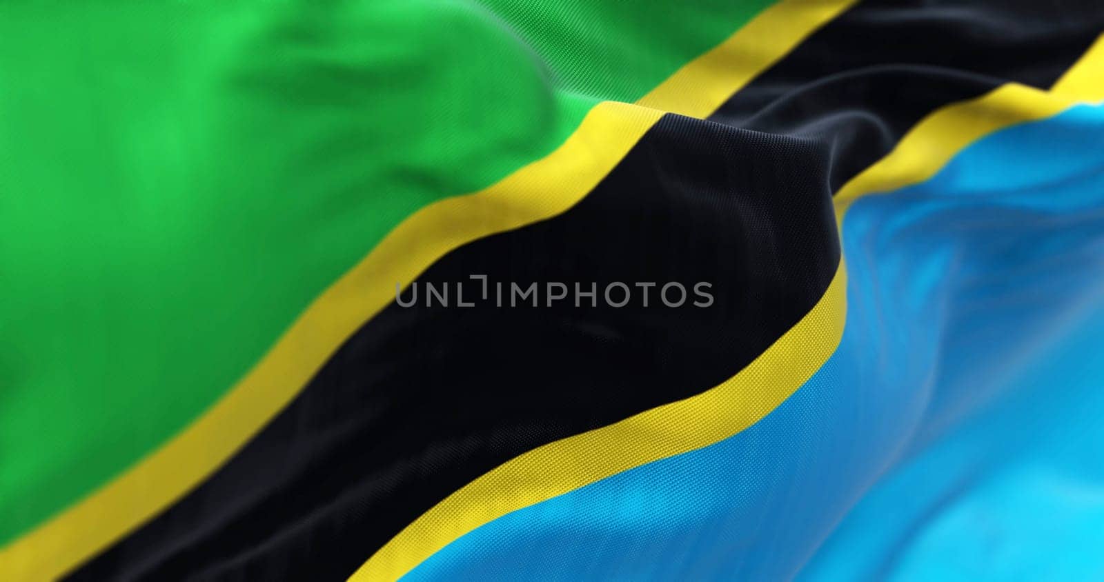 Close-up view of the Tanzania national flag waving. Green and blue triangles with black diagonal stripe and yellow edges. Fabric textured background. Selective focus. 3d illustration render