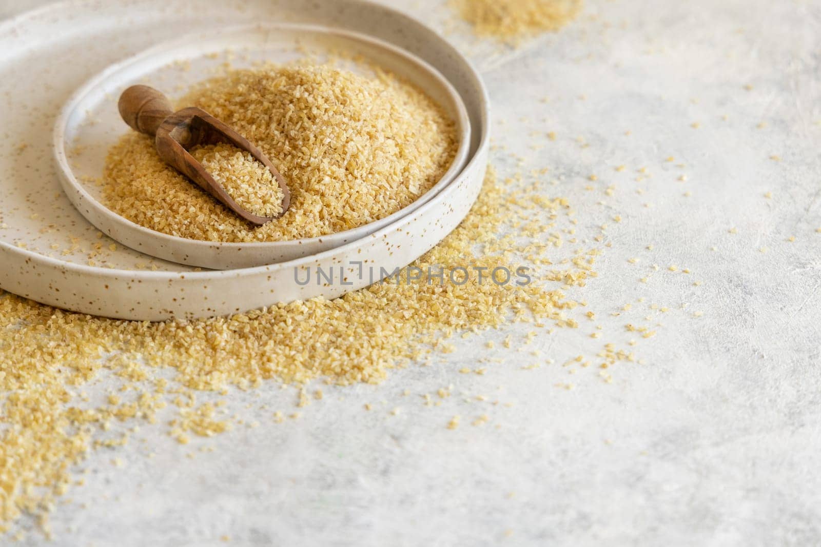 Pile of Dry uncooked bulgur wheat grain with a scoop on a plate close up, copy space. Vegetarian and Vegan, Mediterranean and Middle Eastern cuisine. Healthy lifestyle