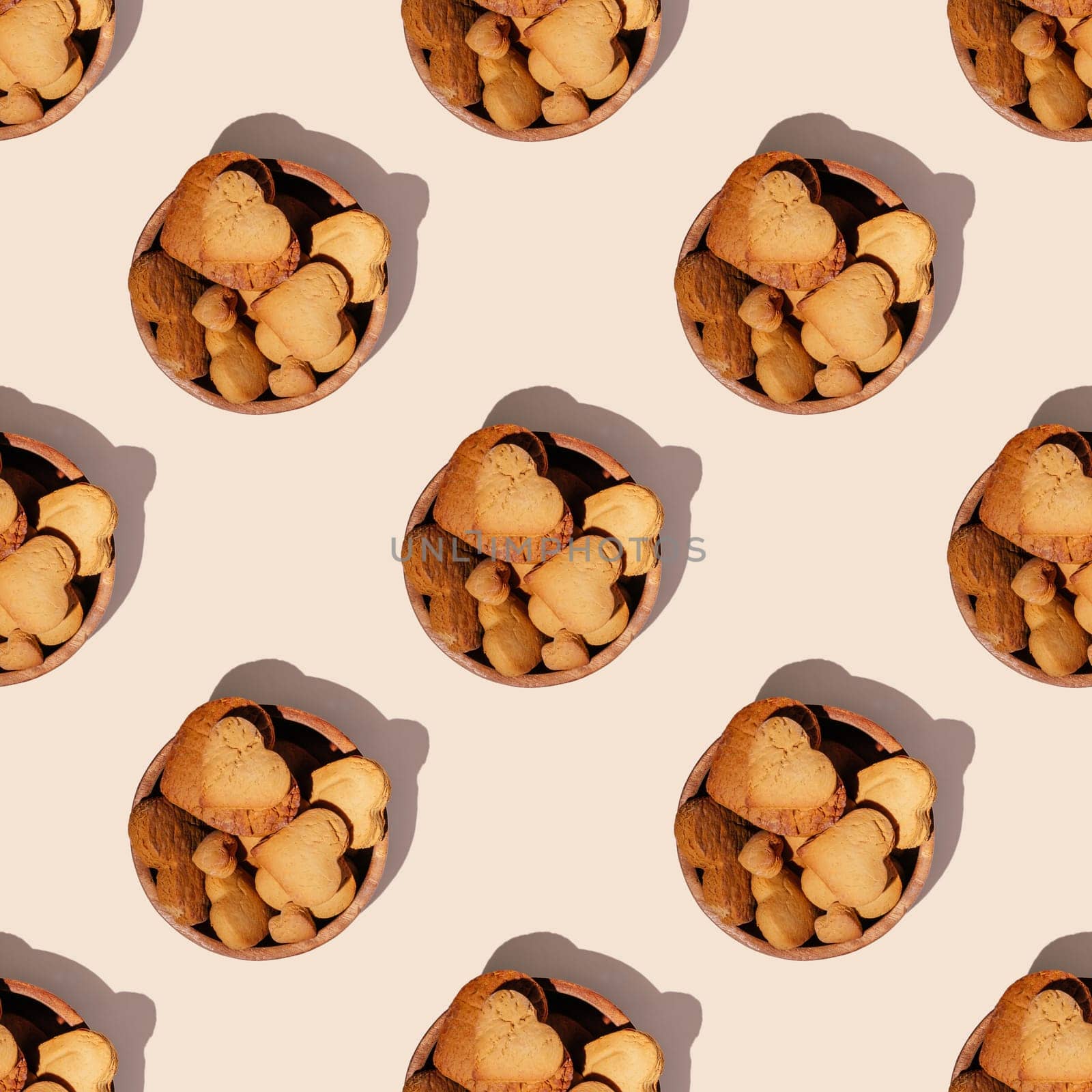 Seamless endless pattern of heart shaped gingerbread cookies in wooden bowl with hard shadows isolated on light pink background. Top view
