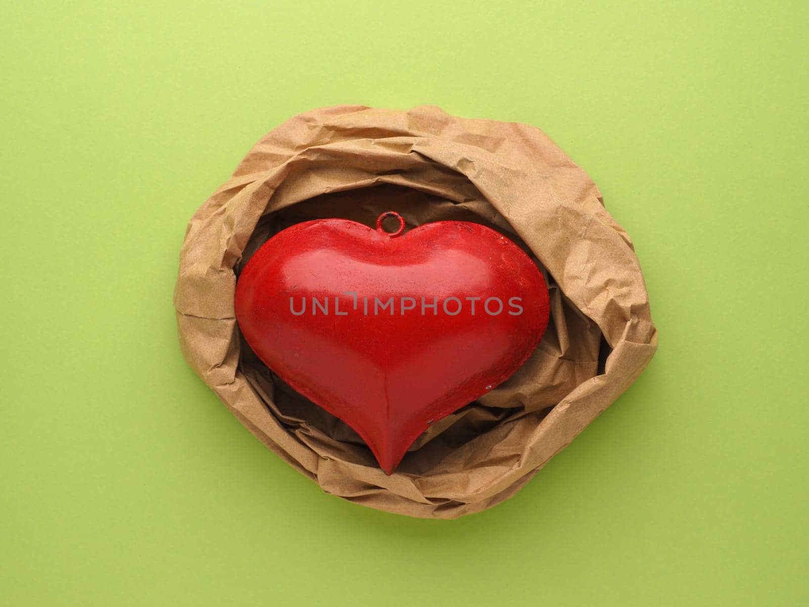 Red metal heart decoration on crumpled beige paper and red paper background with space for text