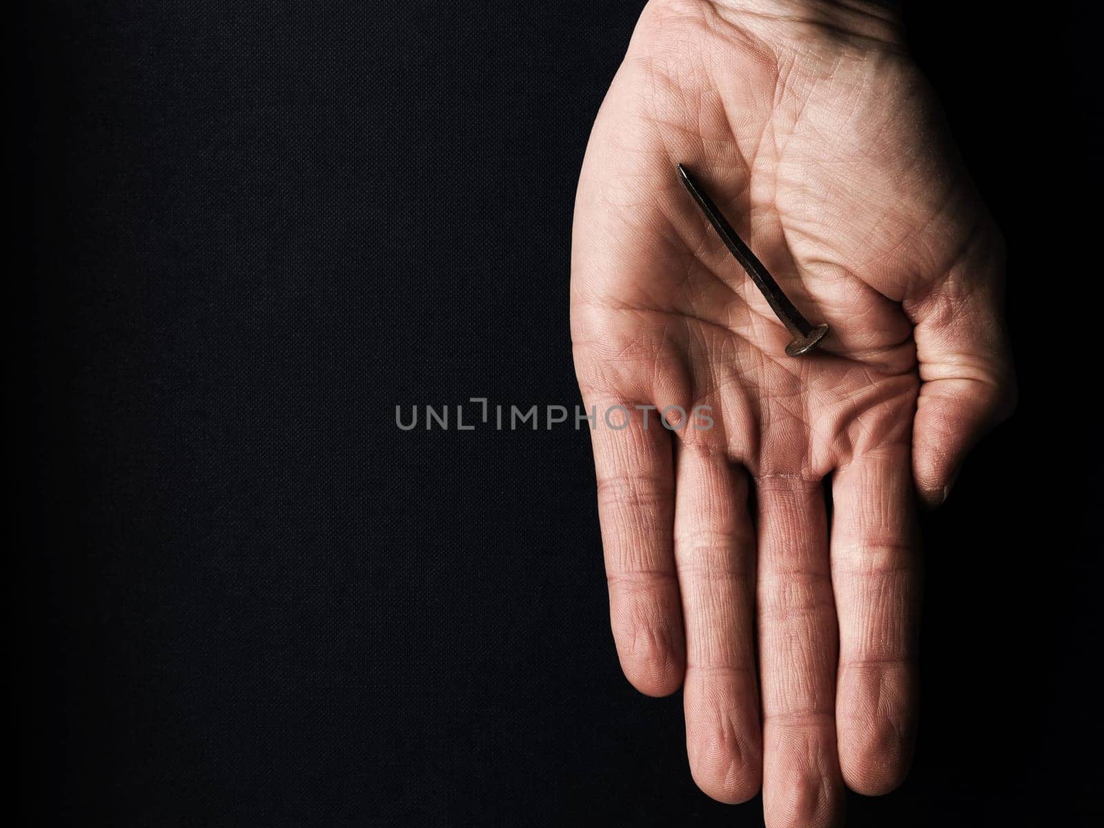 Hand with an old rusty nail symbolizes the crucifixion of Jesus. Easter concept with text free space