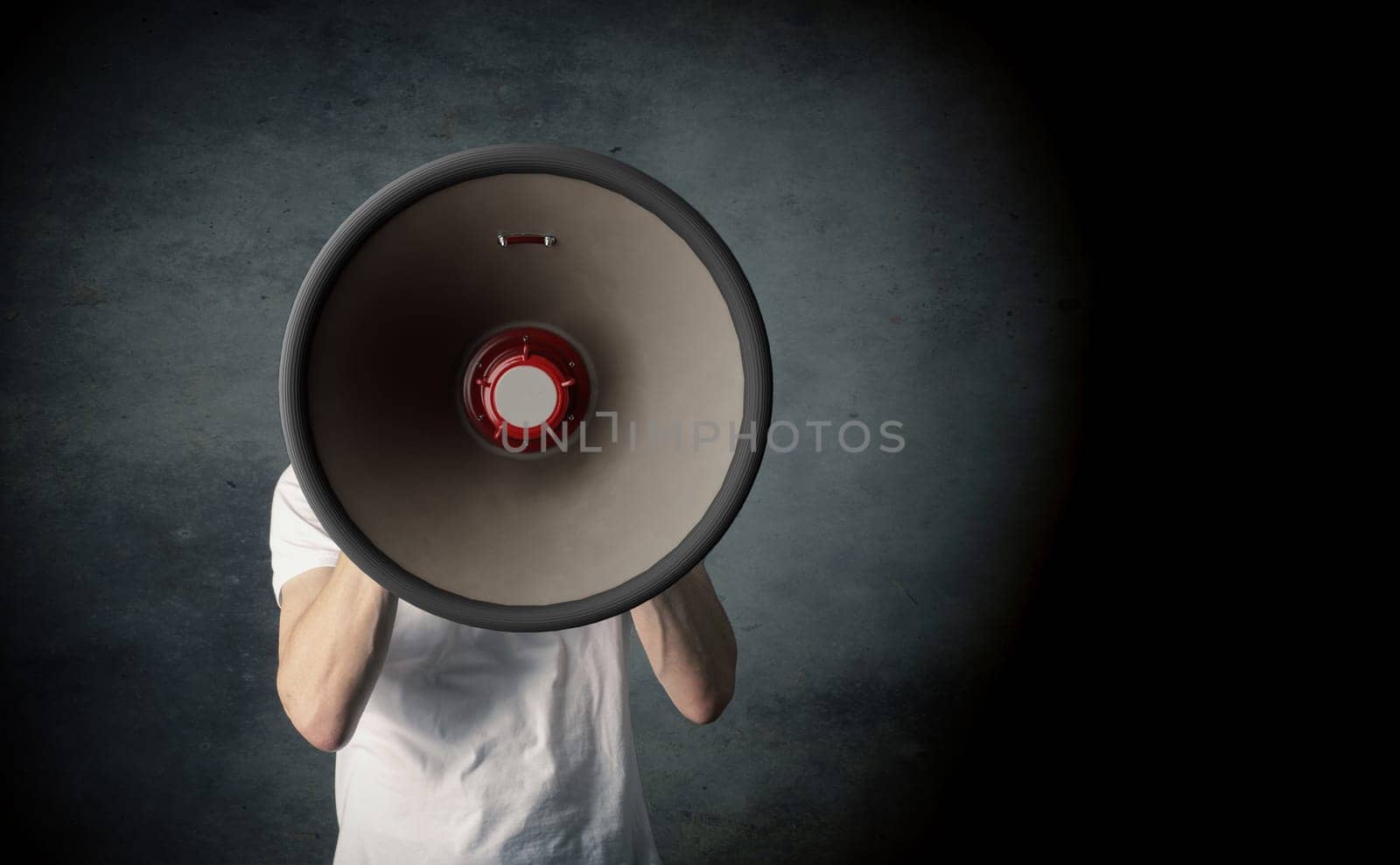 Young man holding a big megaphone, speaking loud concept on a dark studio background with space for your text or image