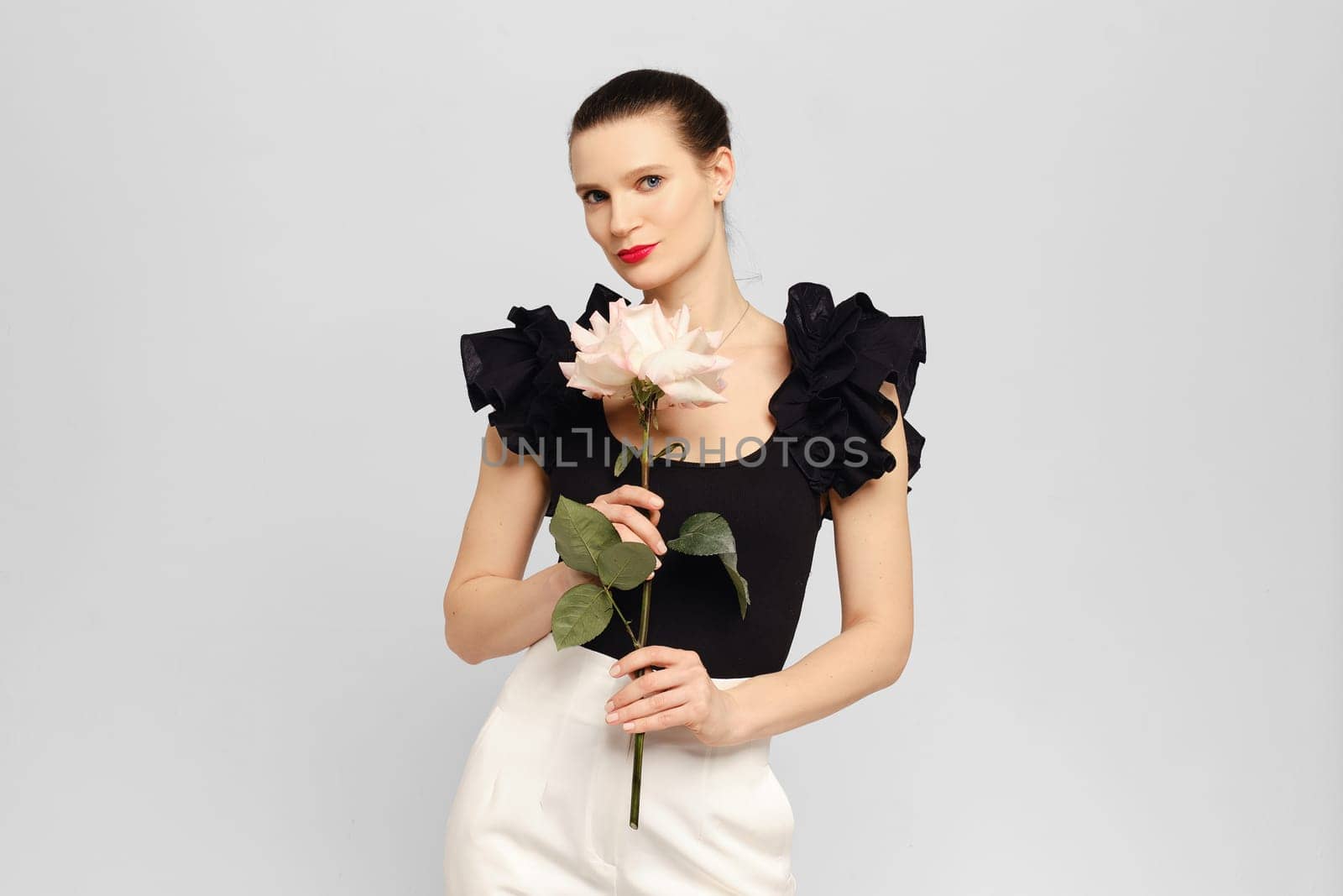 Stylish and positive adult woman posing in white studio with rose in hands