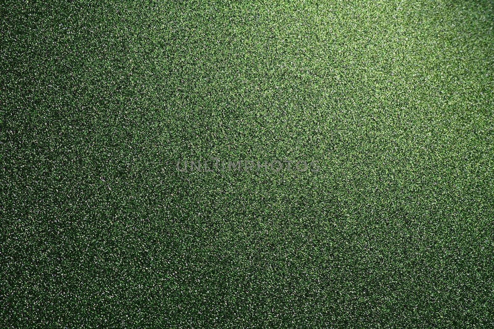 Deep grassy green. Texture of rough paper or cardboard. Defocused bokeh sparkles and shine on the fold. Festive green background with illuminated gradient from top right