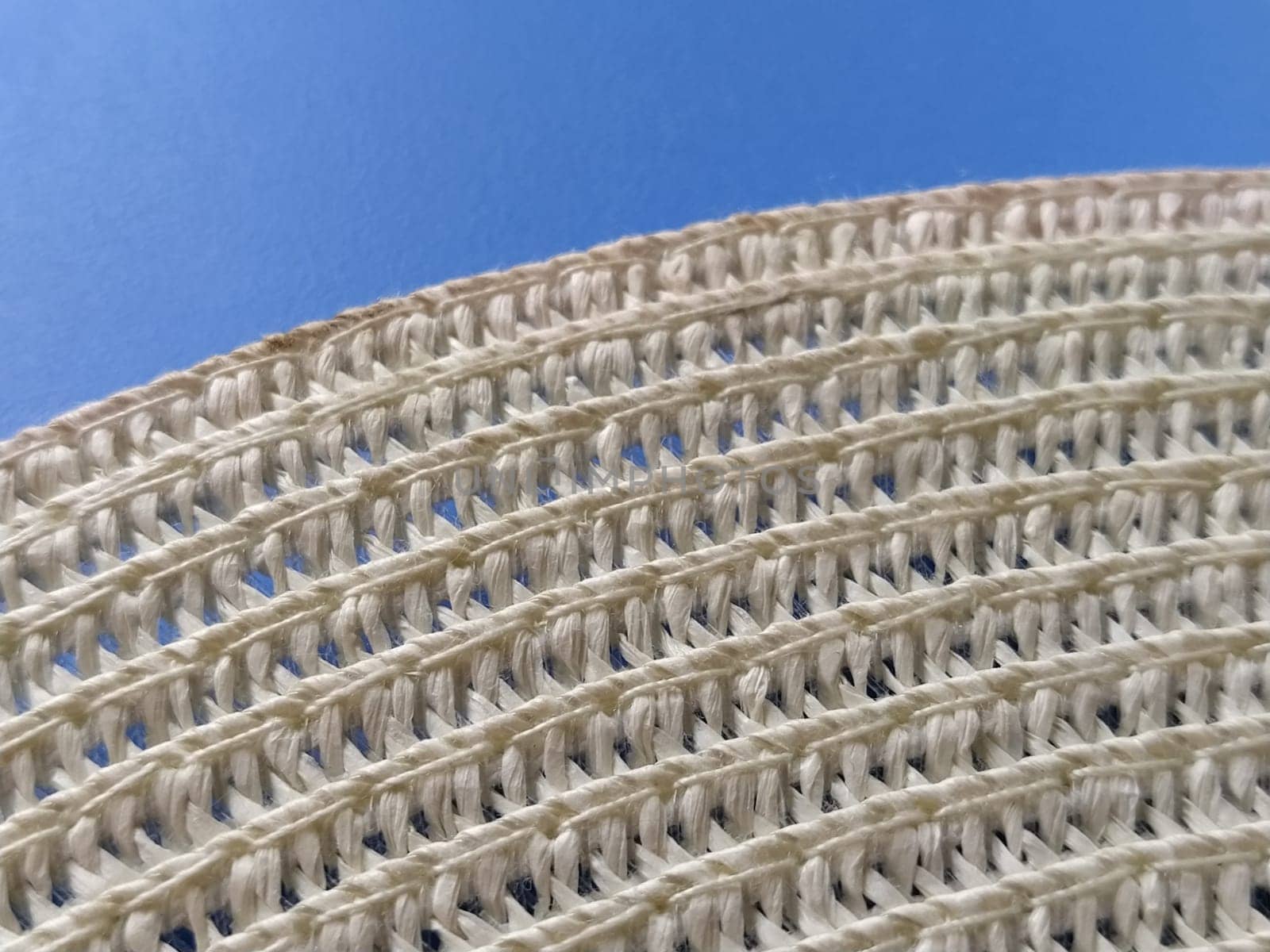 Straw hat on a blue background. The edge of the wide brim of the hat. Weave threads or twigs. Close-up. Summer holiday theme.