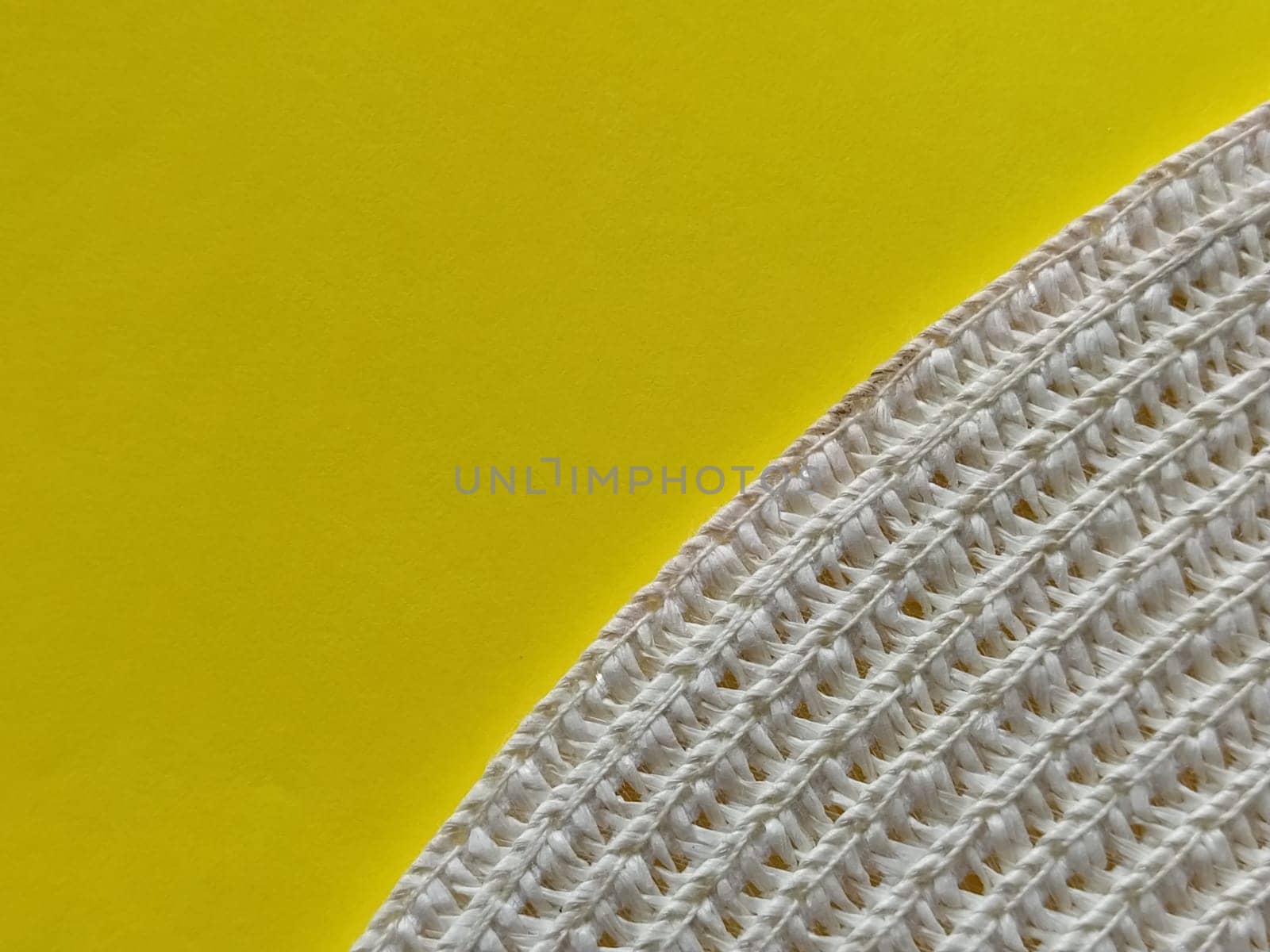 Straw hat on a yellow background. The edge of the wide brim of the hat. Weave threads or twigs. Close-up. Summer holiday theme.