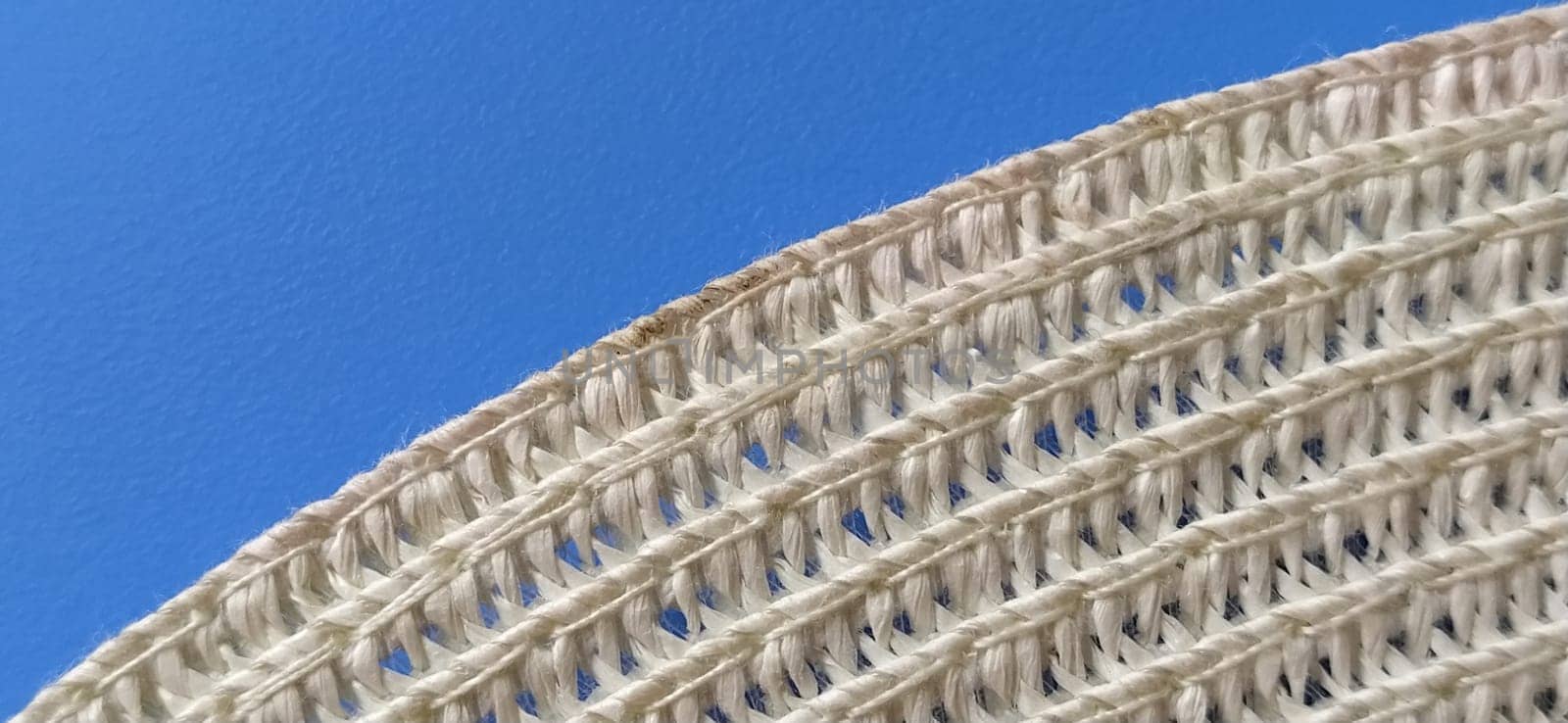 Straw hat on a blue background. The edge of the wide brim of the hat. Weave threads or twigs. Close-up. Summer holiday theme. Banner.