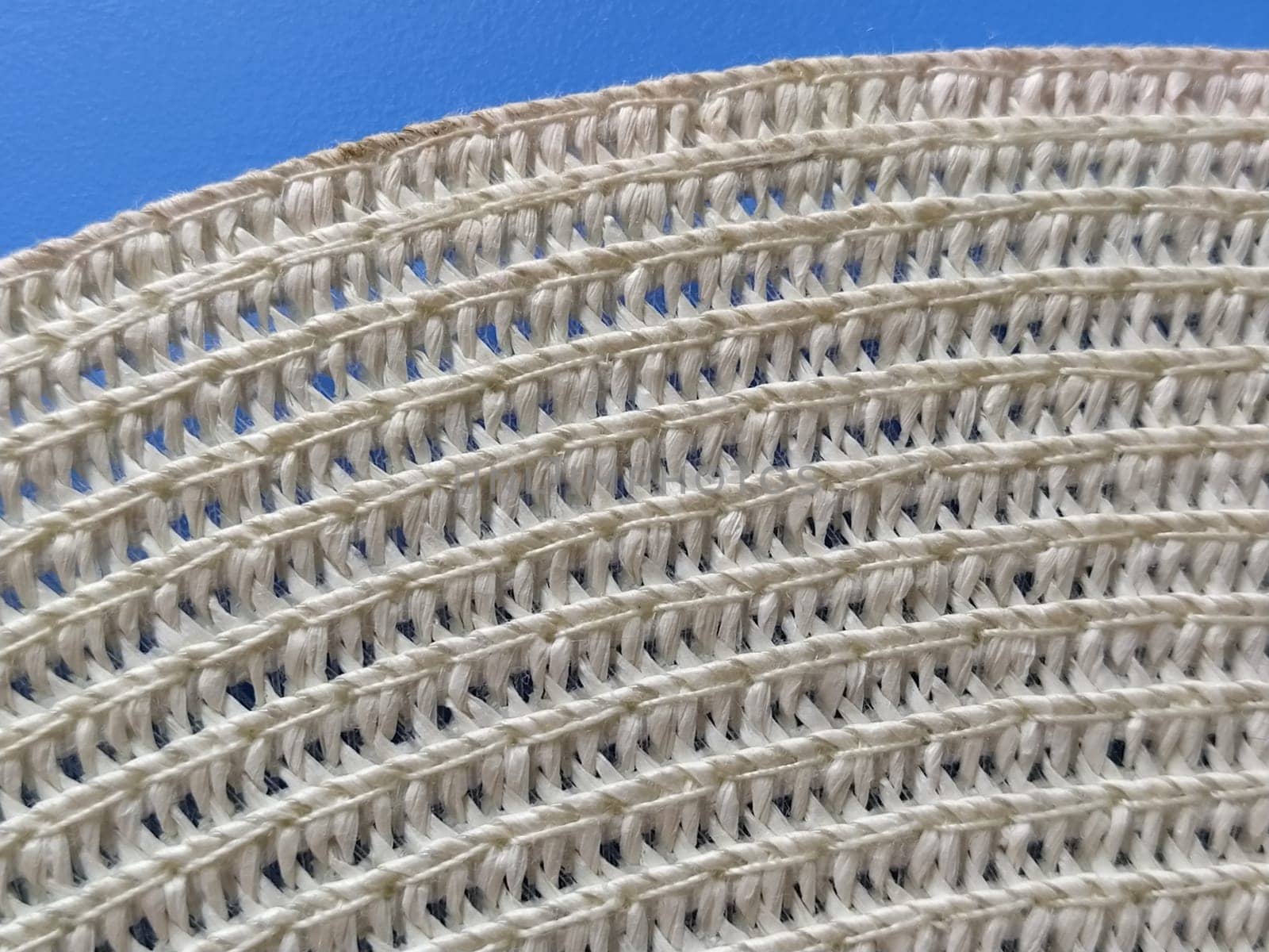 Straw hat on a blue background. The edge of the wide brim of the hat. Weave threads or twigs. Close-up. Summer holiday theme.
