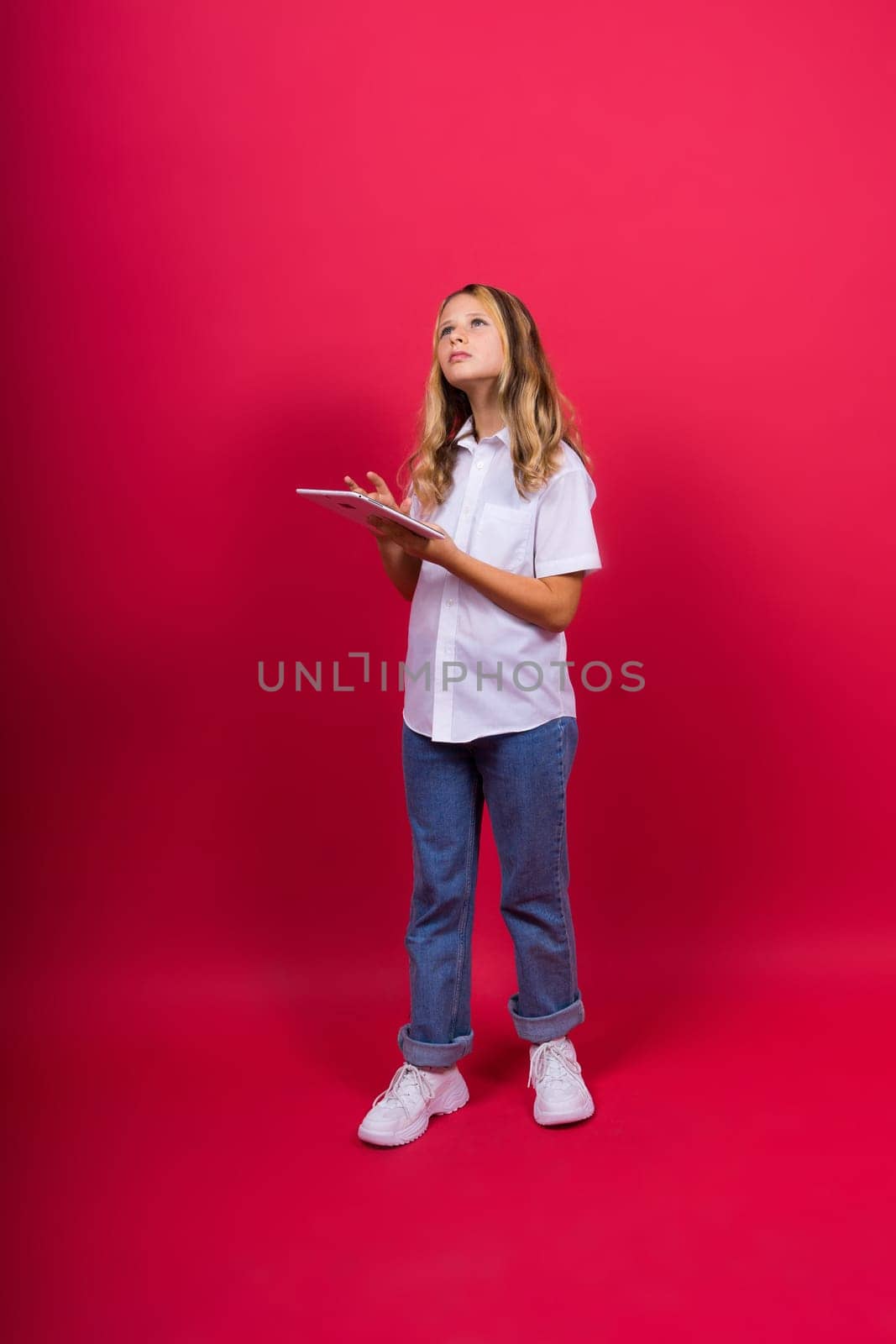 Online school app. Schoolgirl showing tablet computer Empty Screen On red Background. Studio Shot