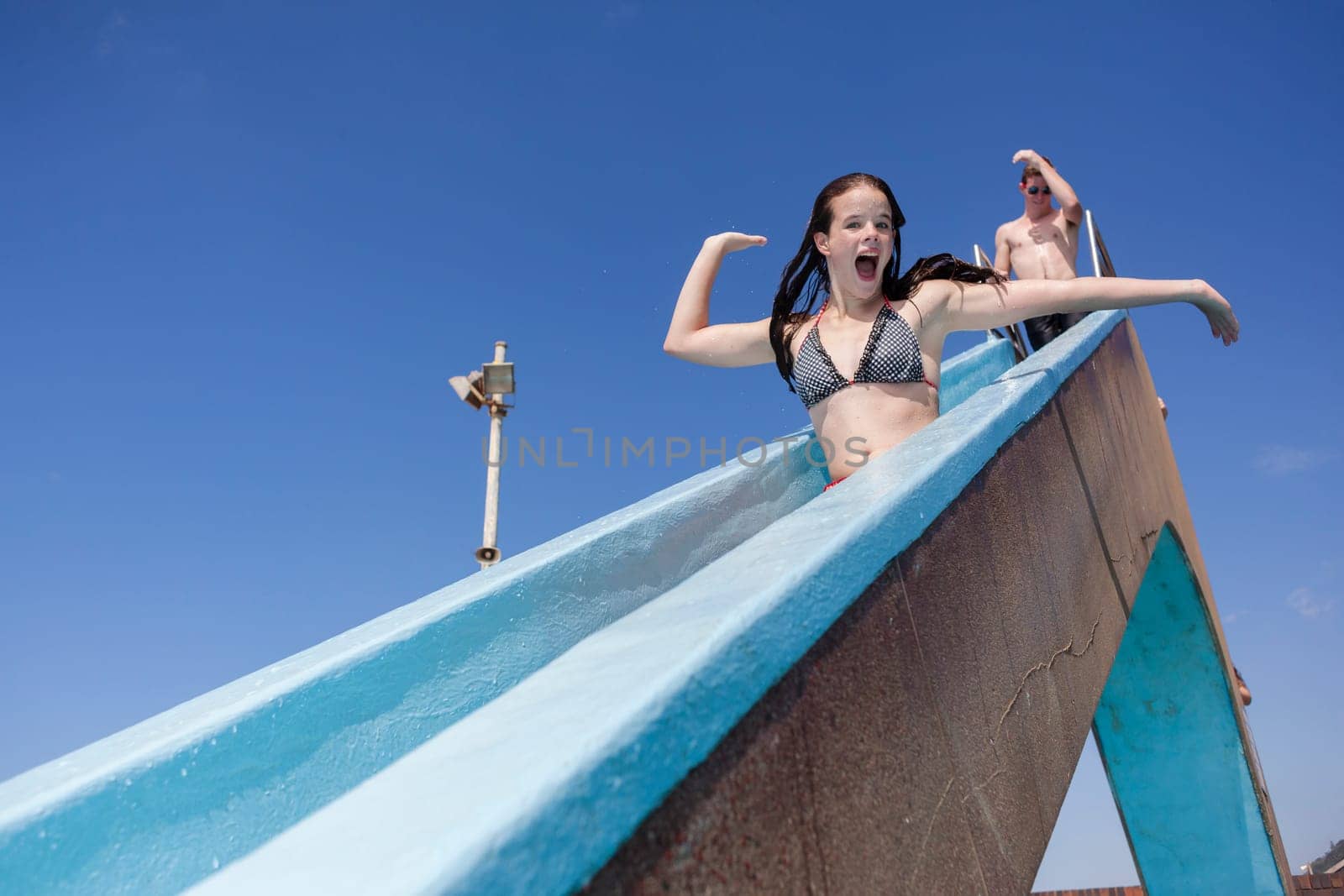 Girl teenager on swimming pool water slide summer fun.