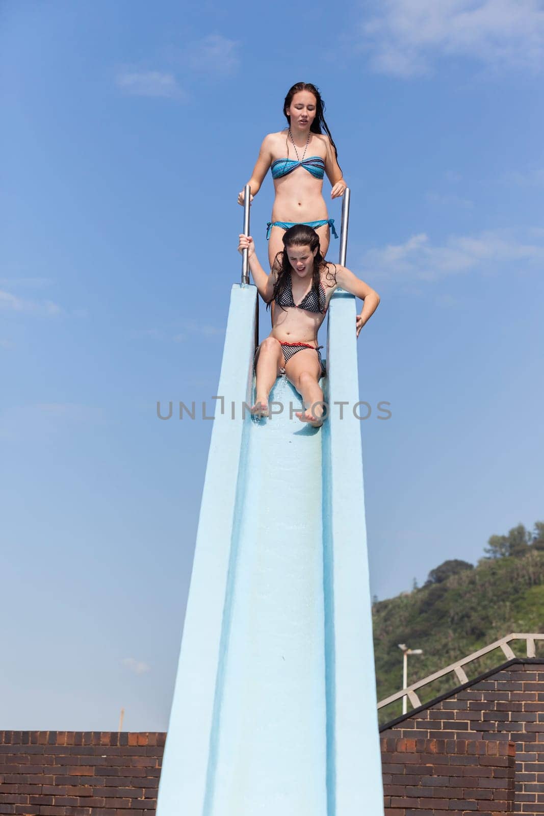 Girl teenager on swimming pool water slide summer fun.