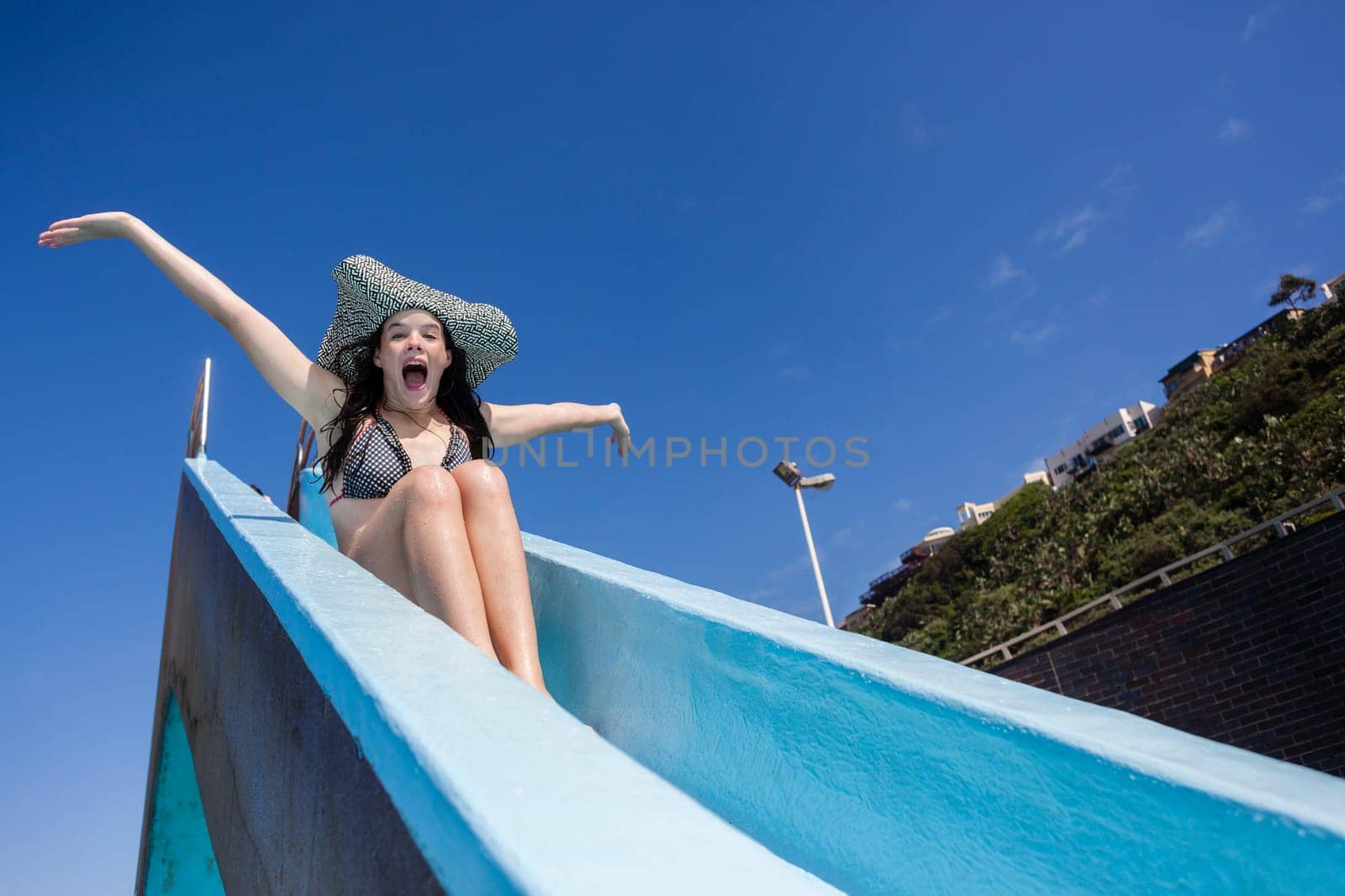 Girl teenager on swimming pool water slide summer fun.