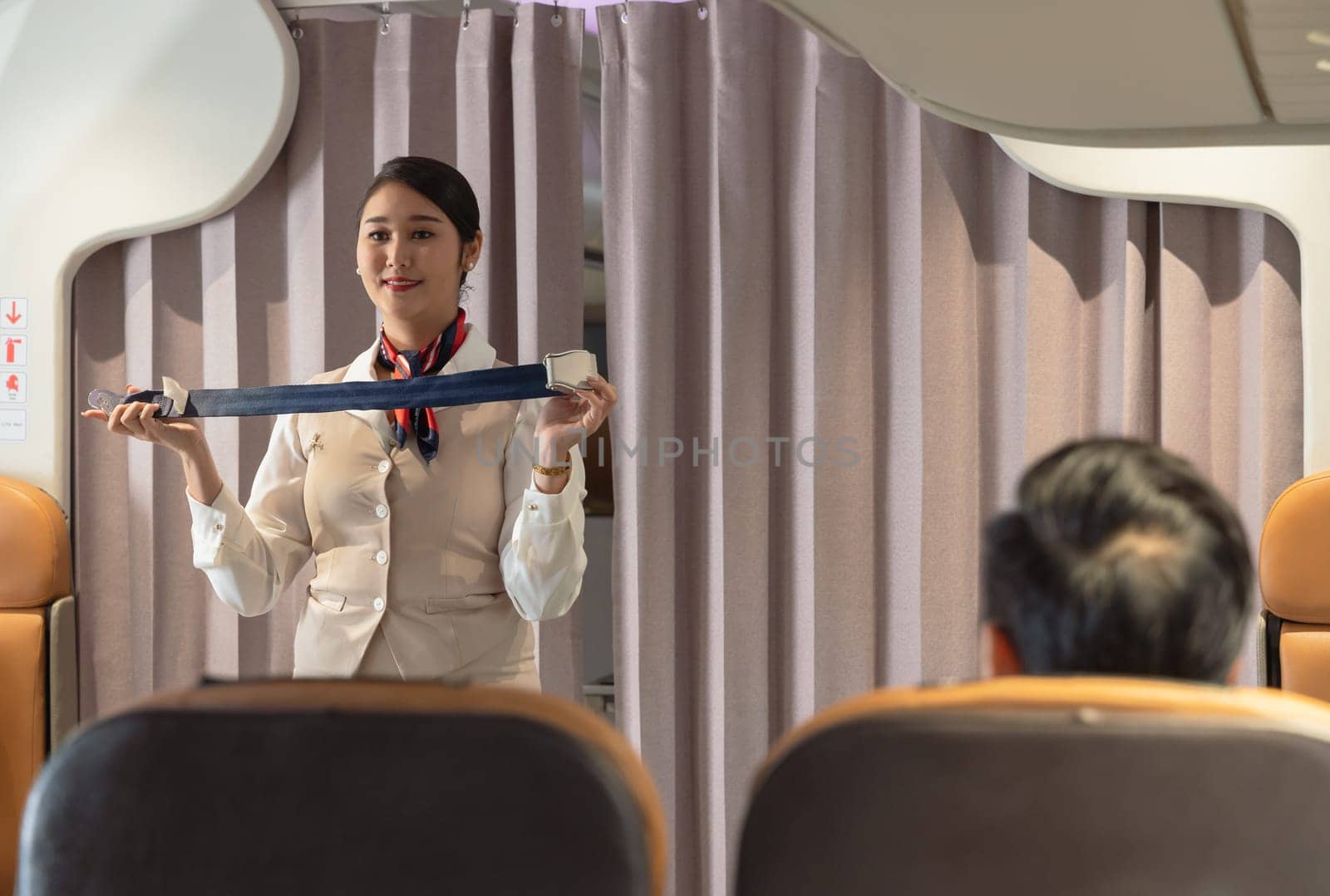 Smiling cheerful flight attendant demonstrating how fastening seat belt to passengers on airplane cabin