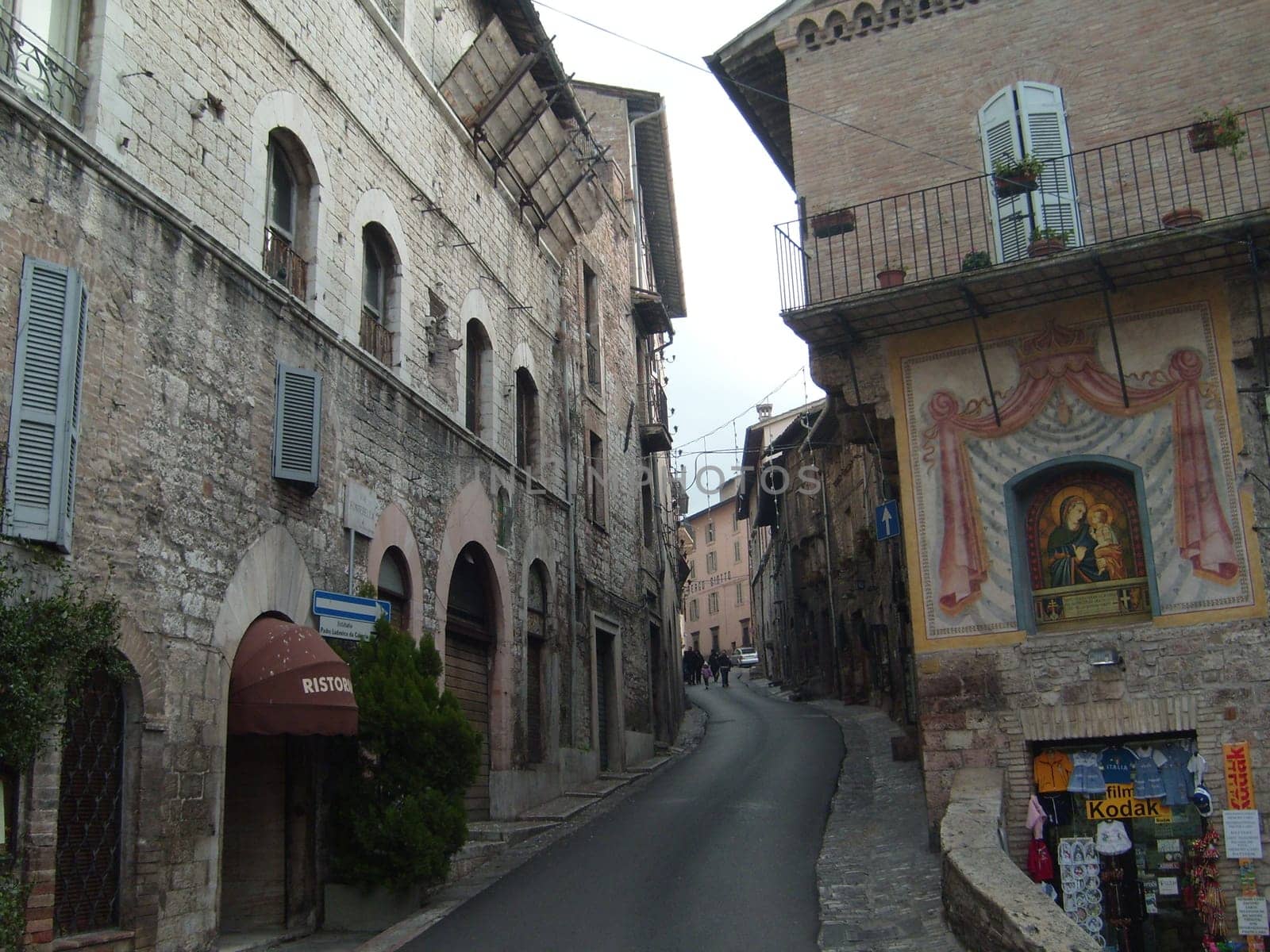 Assisi, Italy, December 10, 2020. Streets of Assisi, along which a group of tourists walk. Ancient buildings, close to each other. People on excursions. Narrow street.