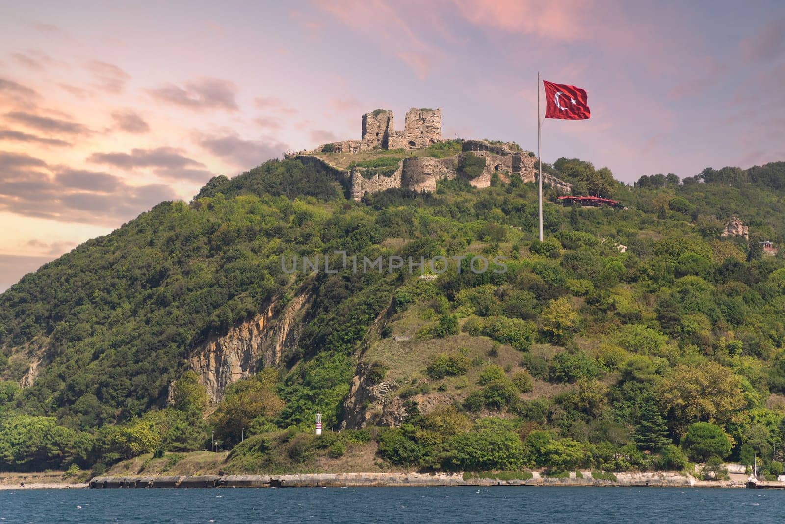 Green mountains of Bosphorus Strait at Anadolu Kavagi, with ruins of Yoros Castle, Yoros Kalesi, or Genoese Castle, at the far end, an ancient Byzantine castle,and huge Turkish flag, Istanbul, Turkey