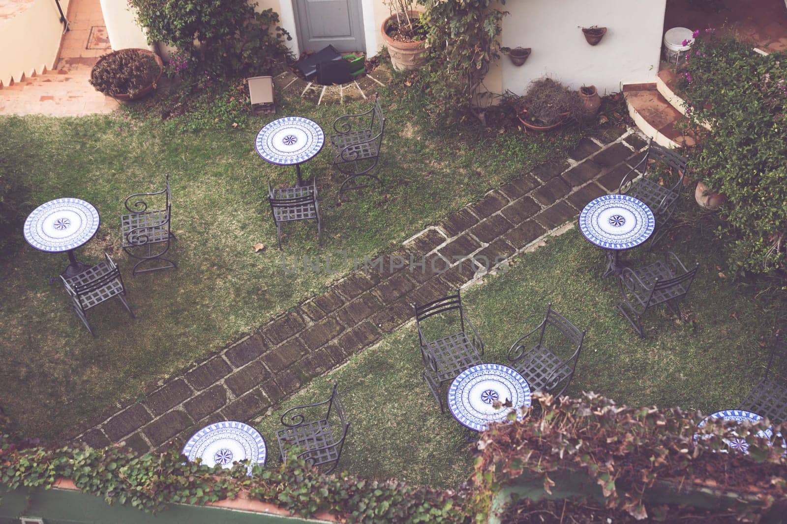 Vintage terrace patio with table and rattan chairs surrounded by lush greenery, high angle view. Relaxing area