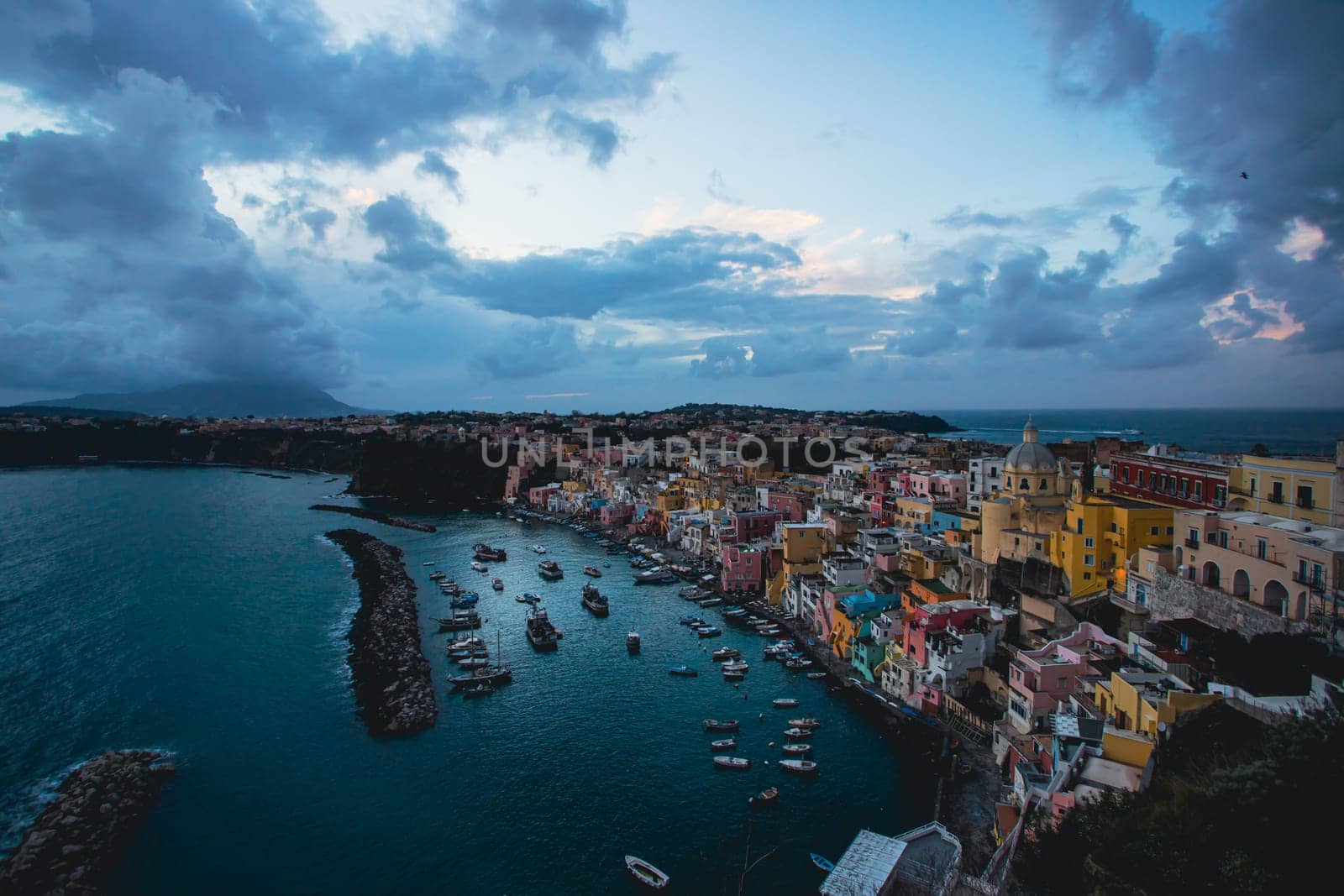 View of the Port of Corricella with lots of colorful houses after sunset in Procida Island, Italy.