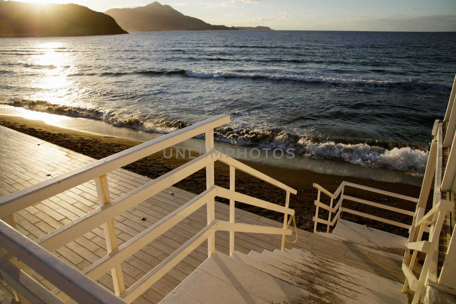 Wooden steps down to beach with waves and sand and island in the sunset.