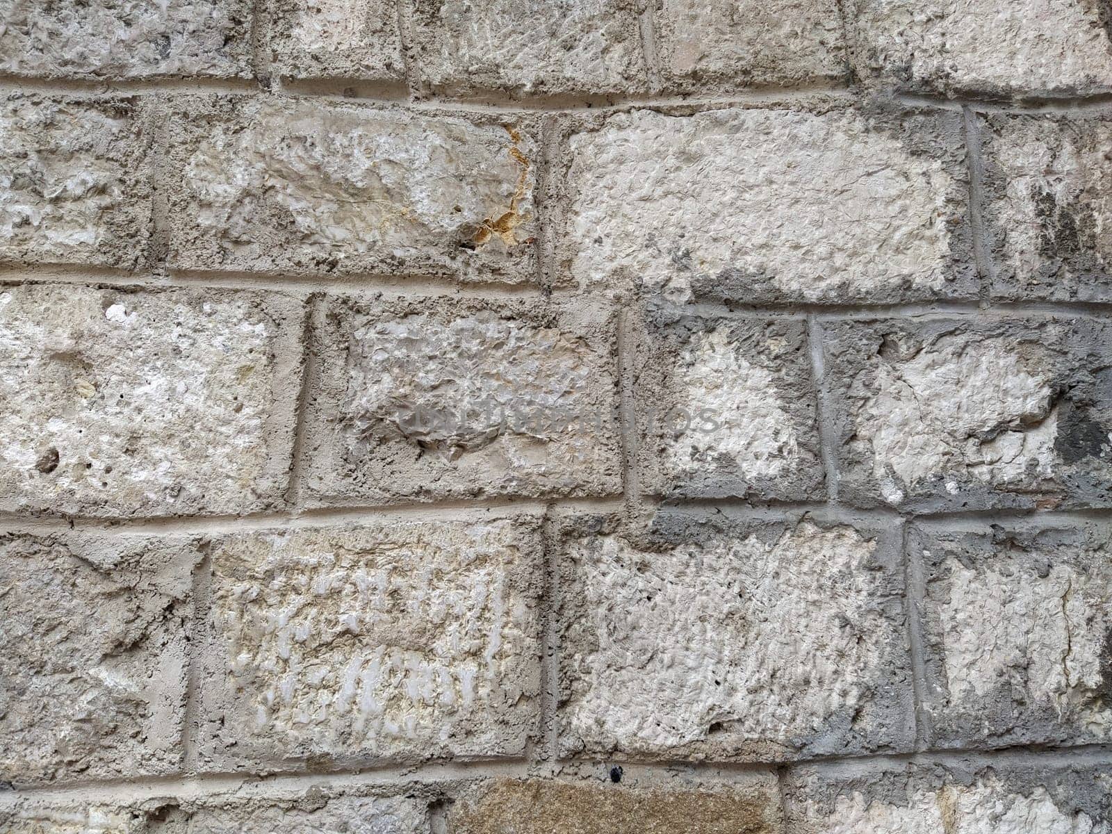 Weathered aged stone masonry of old house. Ancient brick wall background. Old uneven scratched stone bricks texture. Turkish building wall. Rough limestone wall backdrop.