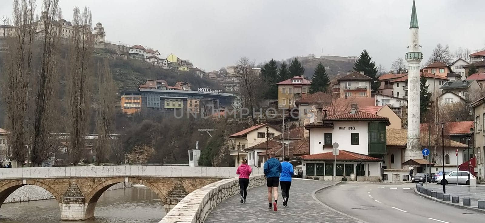 Sarajevo, Bosnia and Herzegovina - March 8, 2020: Sheher bridge over the Milatsk river. Spring. Turbid water in the river and bare trees. Turkish architecture and mosque. Mountains on the horizon.