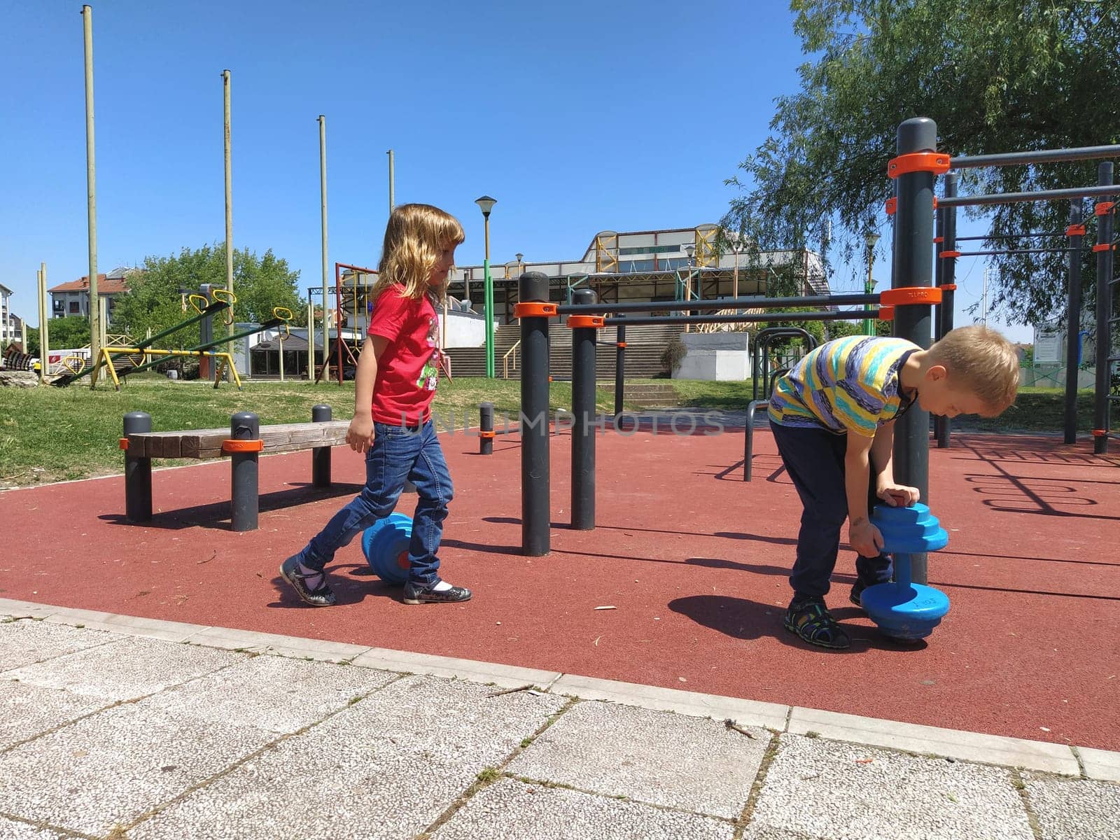 Sremska Mitrovica, Serbia. June 6, 2020. Flip-flops, weight lifting and weights, strength exercises. Two teenagers go in for sports on simulators, children on a sports ground.