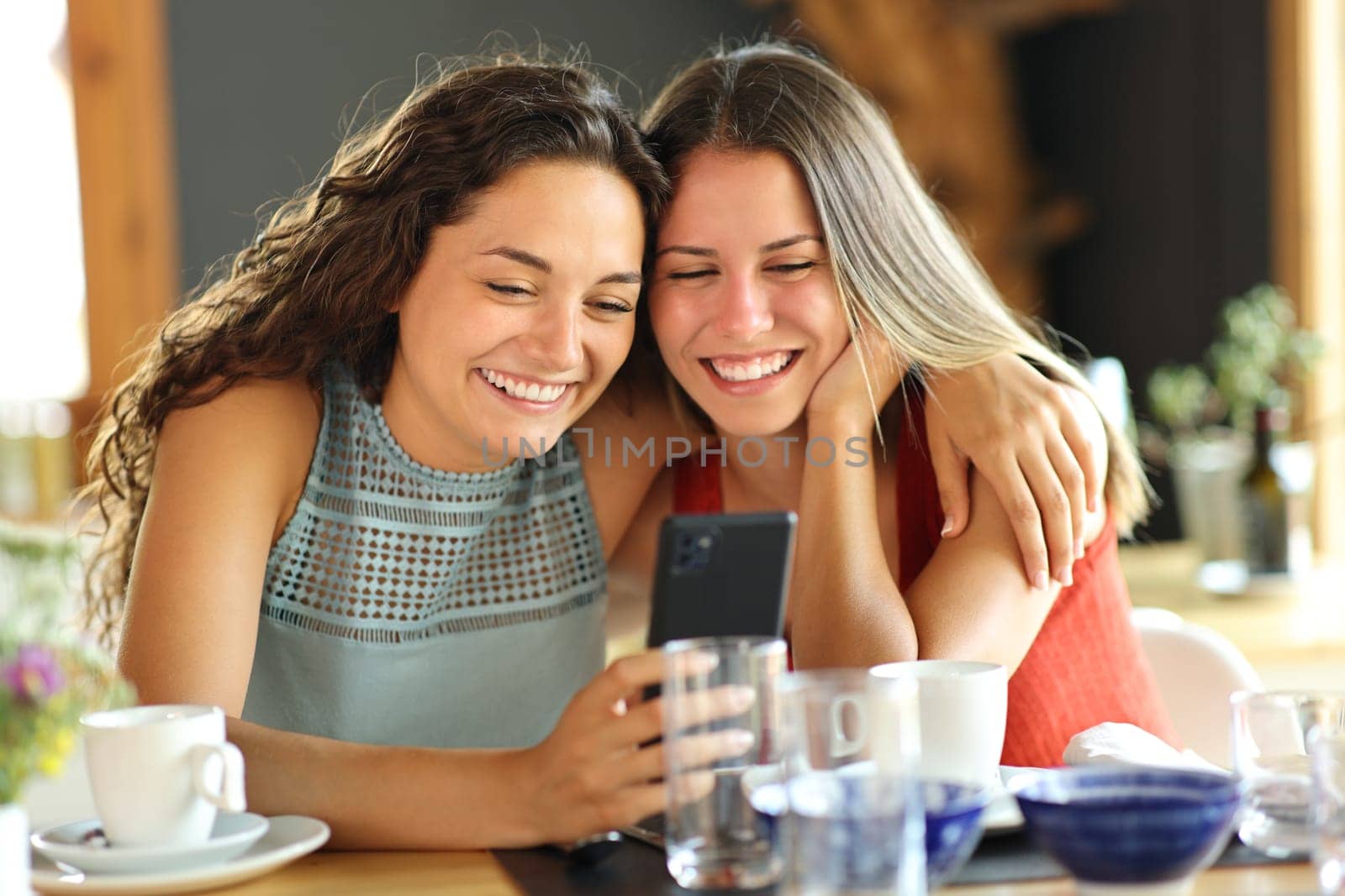 Two happy friends checking cell phone content together in a restaurant