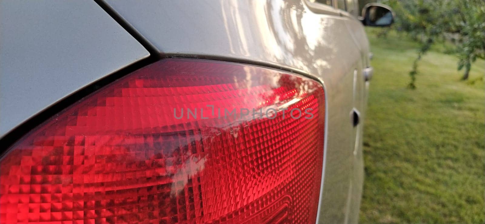 Detail of the rear end of a silver car with focus on the brake lights. Red rear light of the car. Brake signal for the driver driving behind.