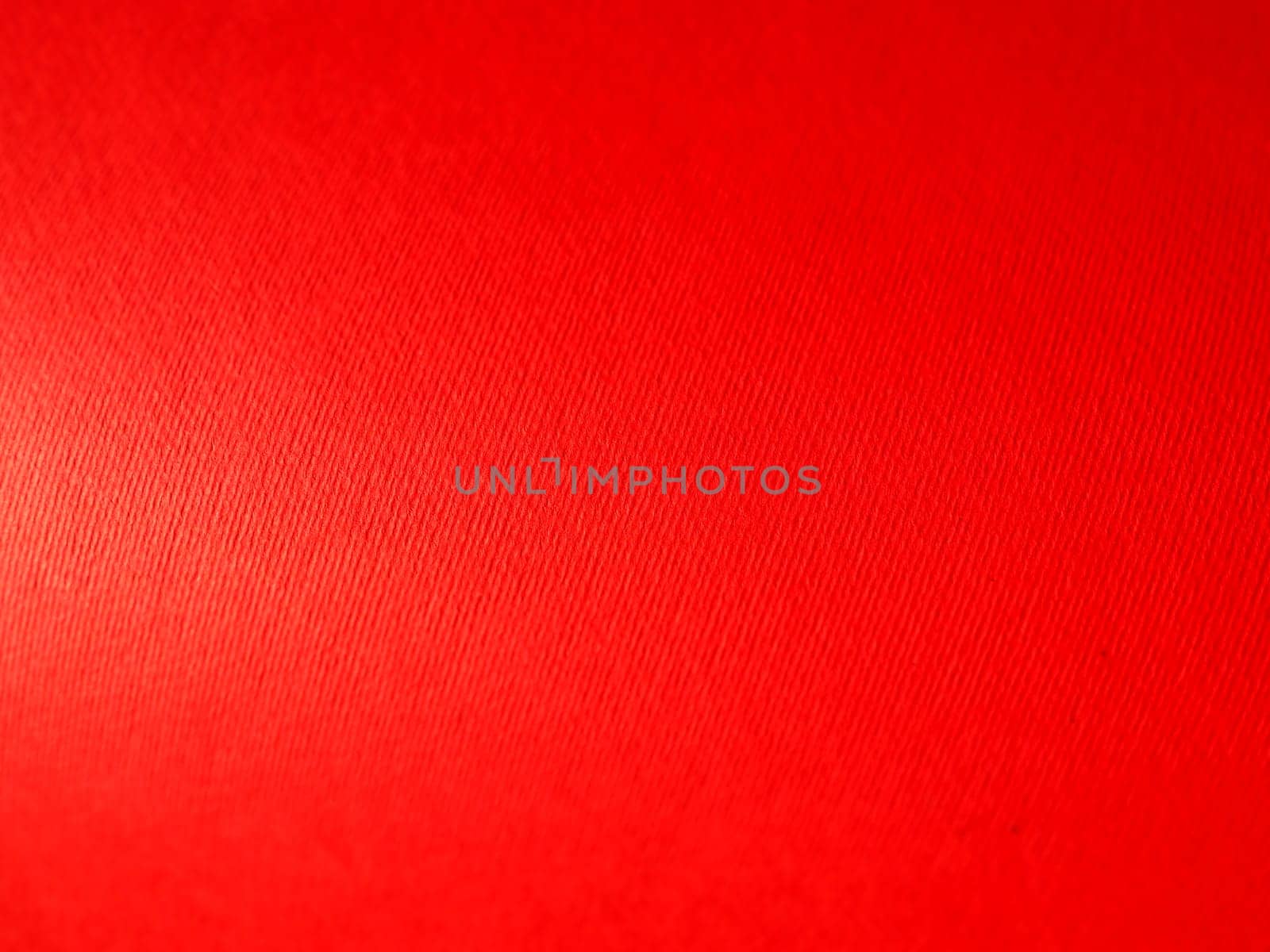 Abstract red background with texture. Close-up of paper surface with light and color gradient. Side lighting. Bright crimson backdrop.
