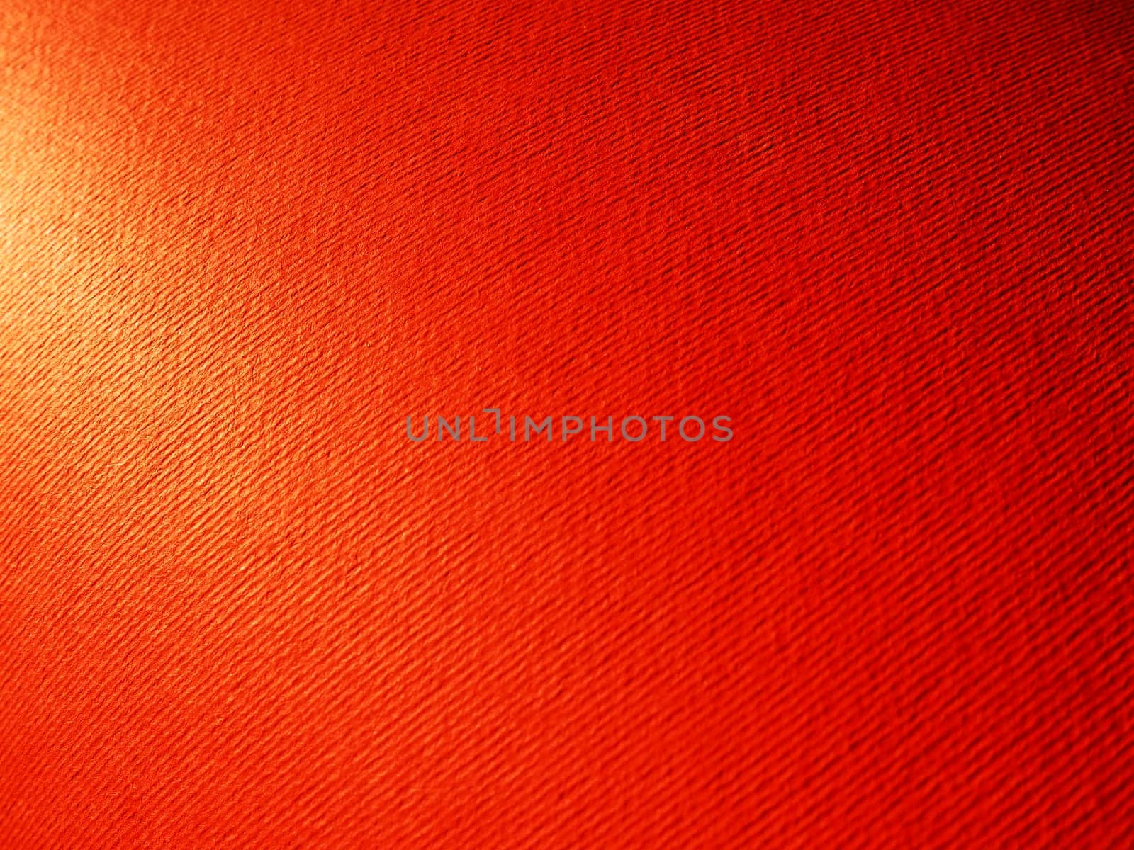 Abstract red background with texture. Close-up of paper surface with light and color gradient. Side lighting. Bright crimson backdrop.