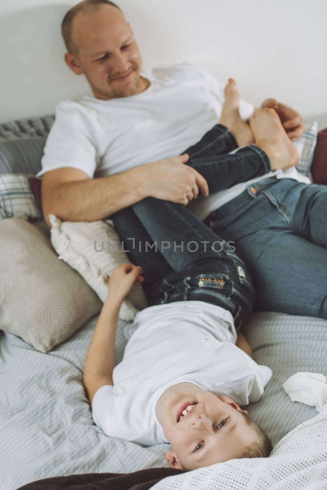 Father plays with his son 7-10 on bed. Dad tickles kids feet. Family having fun