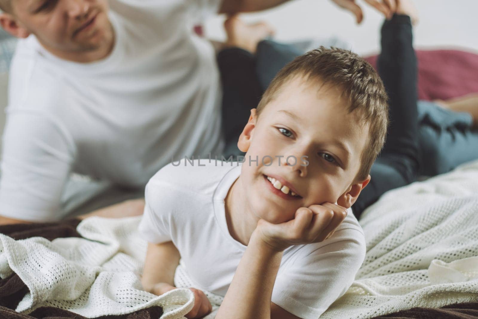 Father plays with his son 7-10 on bed. Dad tickles kids feet. Family having fun