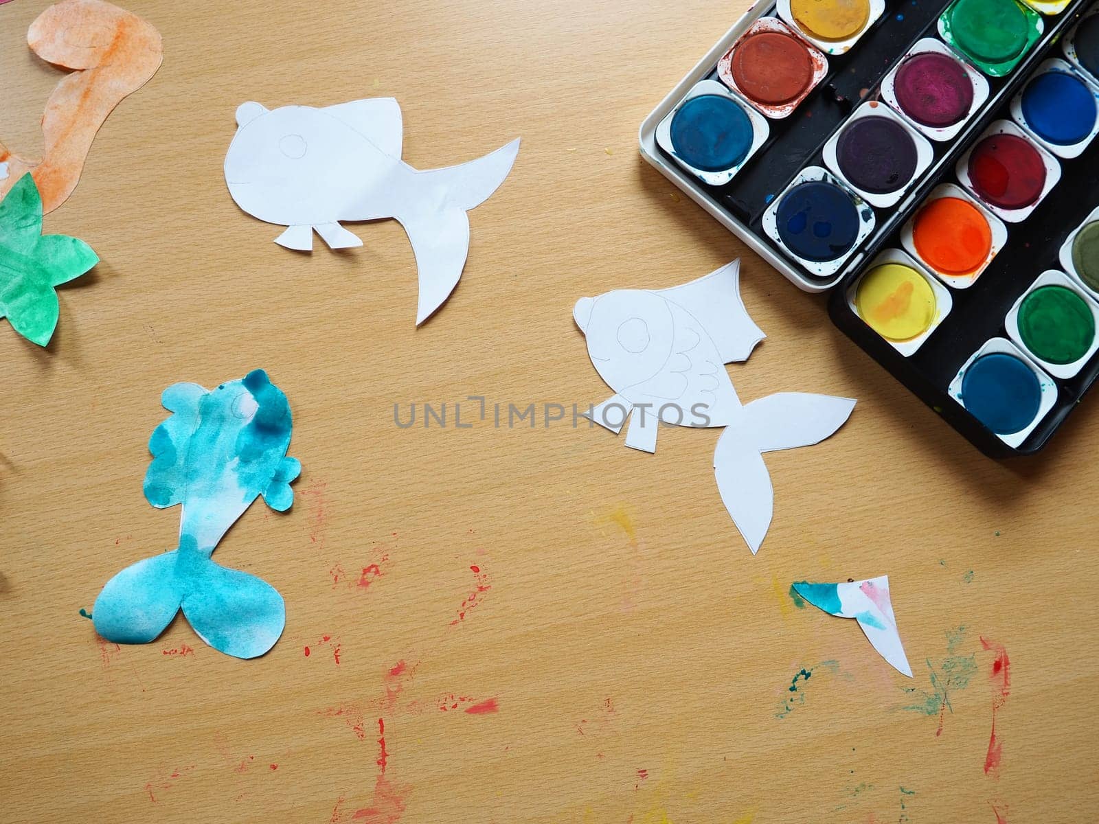 Desktop with drawing tools. A set of watercolor paints. Paper-cut, painted fish figurines. View from above. Lesson or creative task.
