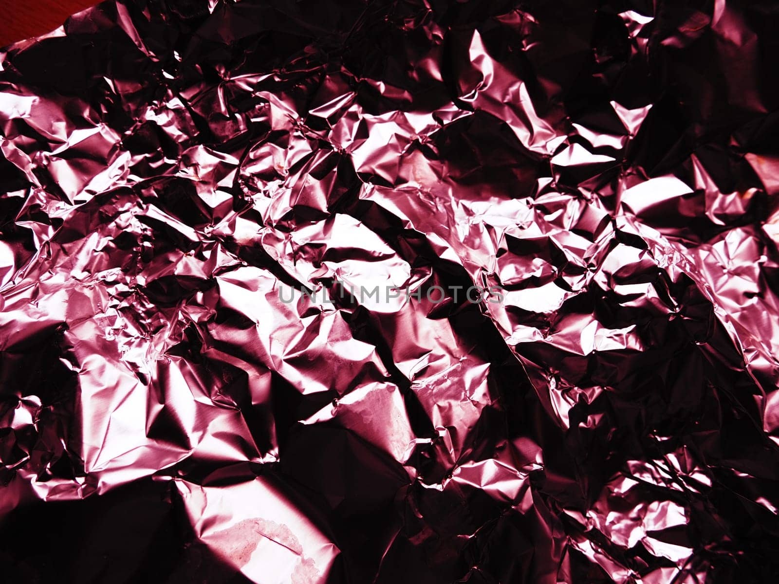 foil close-up. Aluminum silver crumpled foil. Abstract metallic background. Foil for baking food. Background with a red or burgundy tint.