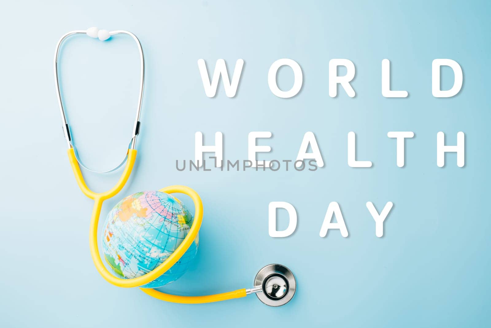 World Health Day. Top view yellow doctor stethoscope wrapped around world globe isolated on pastel blue background with copy space for text, Global healthcare, Health care and medical concept