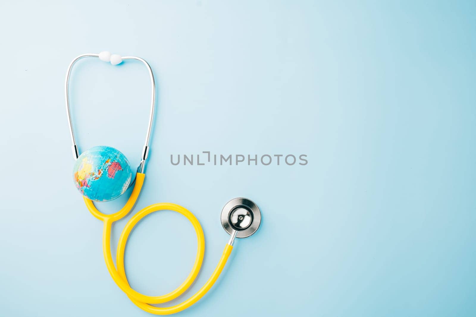 World Health Day. Top view yellow doctor stethoscope wrapped around world globe isolated on pastel blue background with copy space for text, Save world day, Health care and medical concept