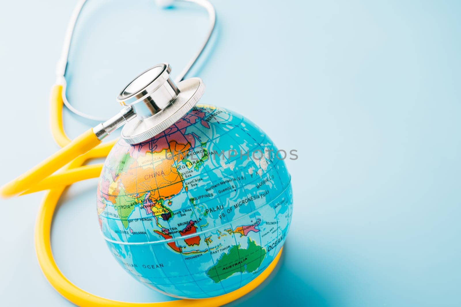 World Health Day. Top view yellow doctor stethoscope wrapped around world globe isolated on pastel blue background with copy space for text, Save world day, Health care and medical concept