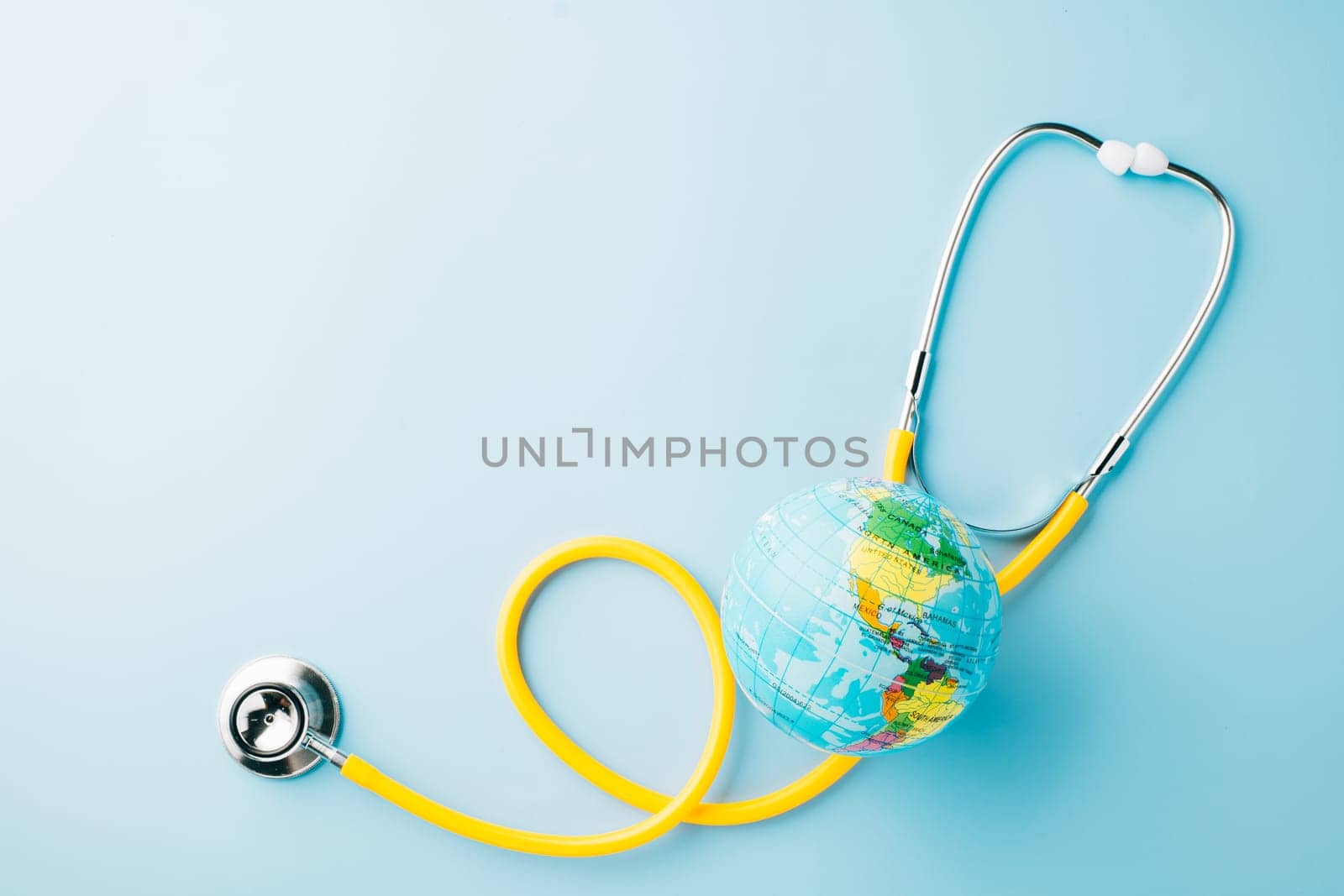 World Health Day Concept. Top view yellow doctor stethoscope and world globe isolated on pastel blue background with copy space, Save world day, Environment Green Earth, Health care and medical