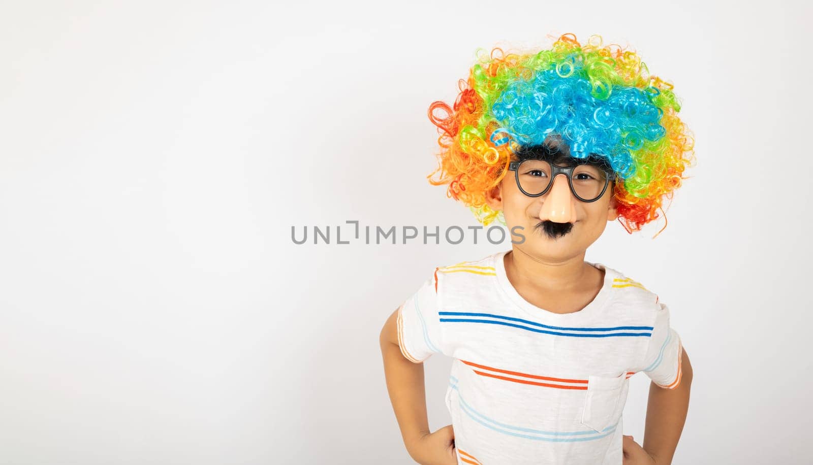April Fool's Day. Portrait of Funny kid boy clown wears a curly wig colorful a big nos and glasses and has a mustache isolated on white background with copy space, Happy child festive decor