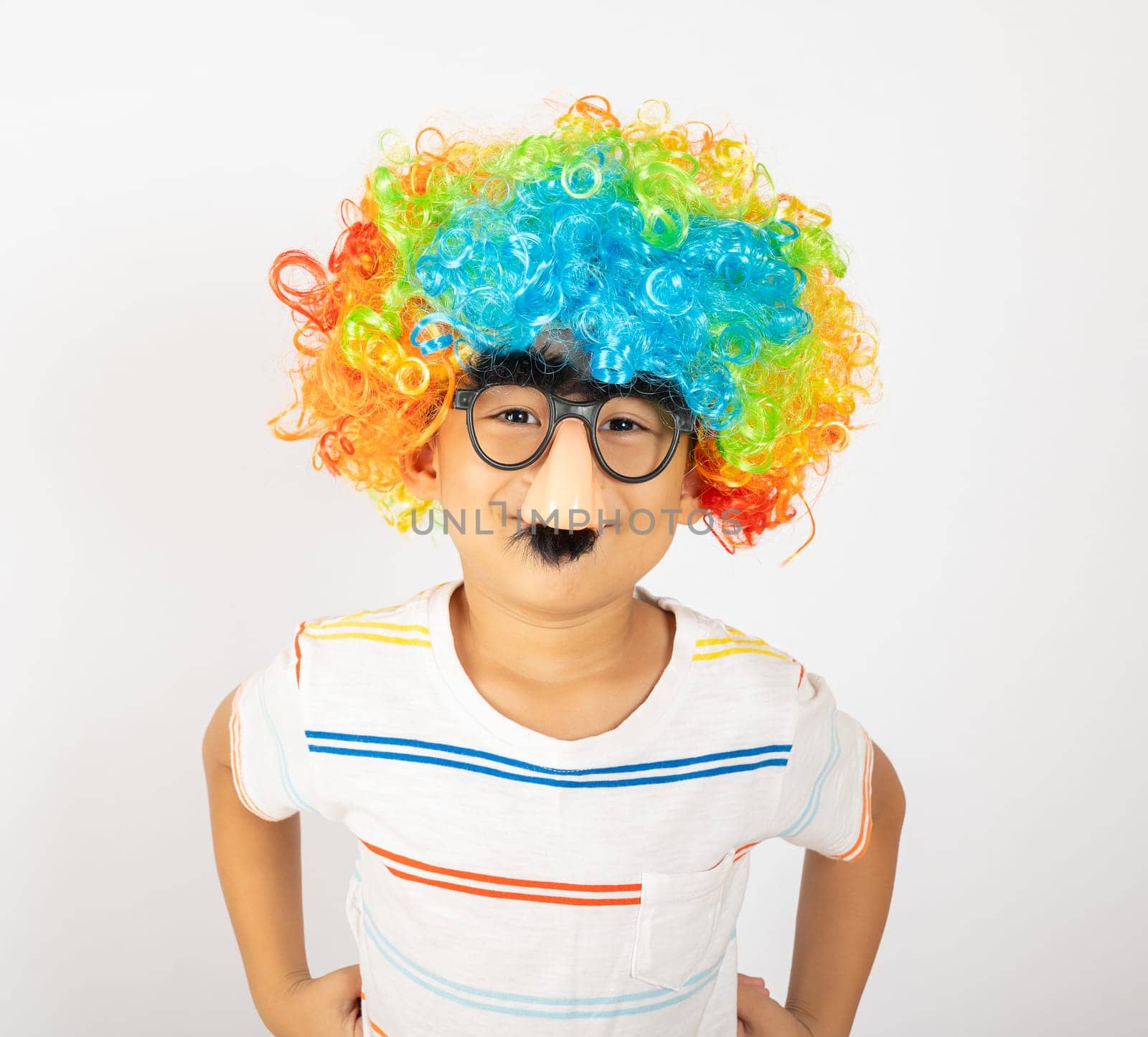 April Fool's Day. Portrait of Funny kid boy clown wears a curly wig colorful a big nos and glasses and has a mustache isolated on white background with copy space, Happy child festive decor