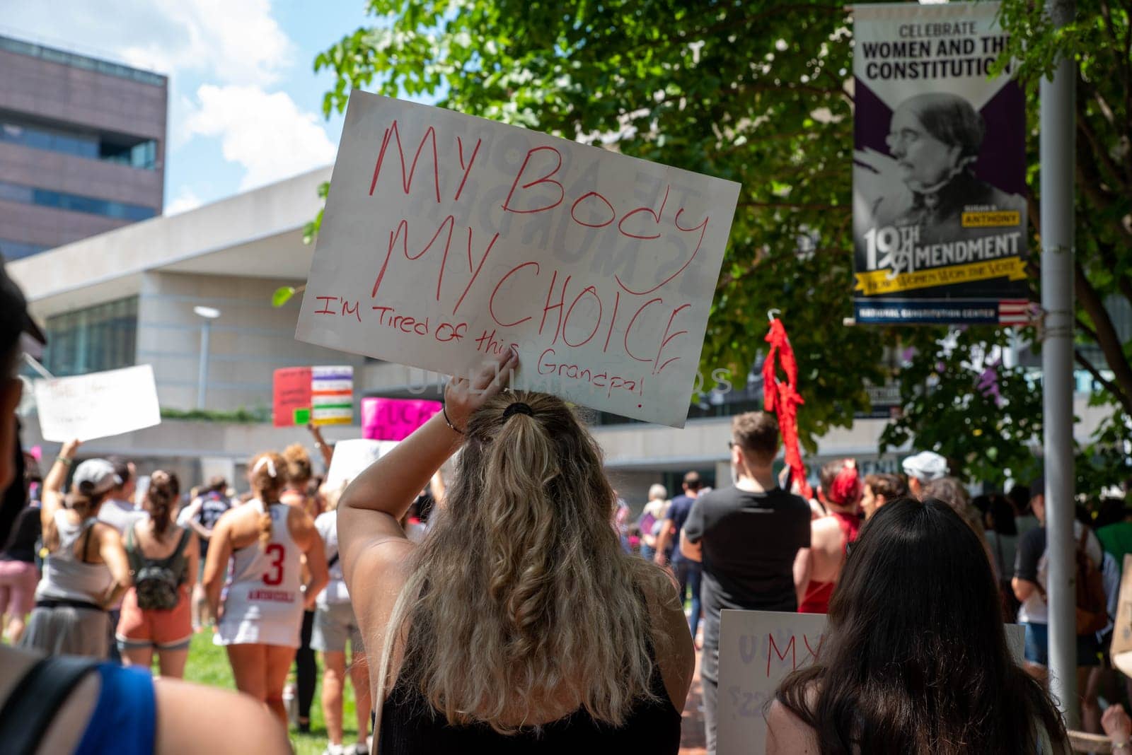 Young woman holds a feminist protest sign over her head in a crowd at a pro-choice political rally. MY BODY MY CHOICE I'M TIRED OF THIS GRANDPA!