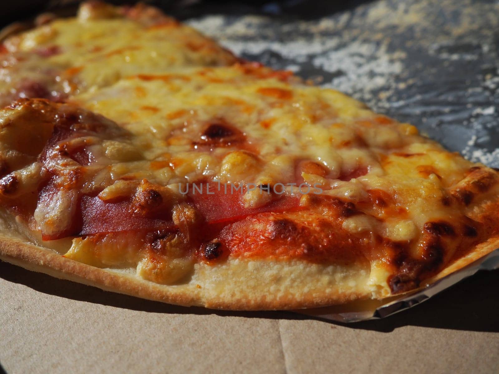 Pizza with tomatoes and cheese in a cardboard box and aluminum foil. Delicious pizza close up. Courier delivery of food to your home. Ordering pizza. Traditional Italian round yeast cake with filling.