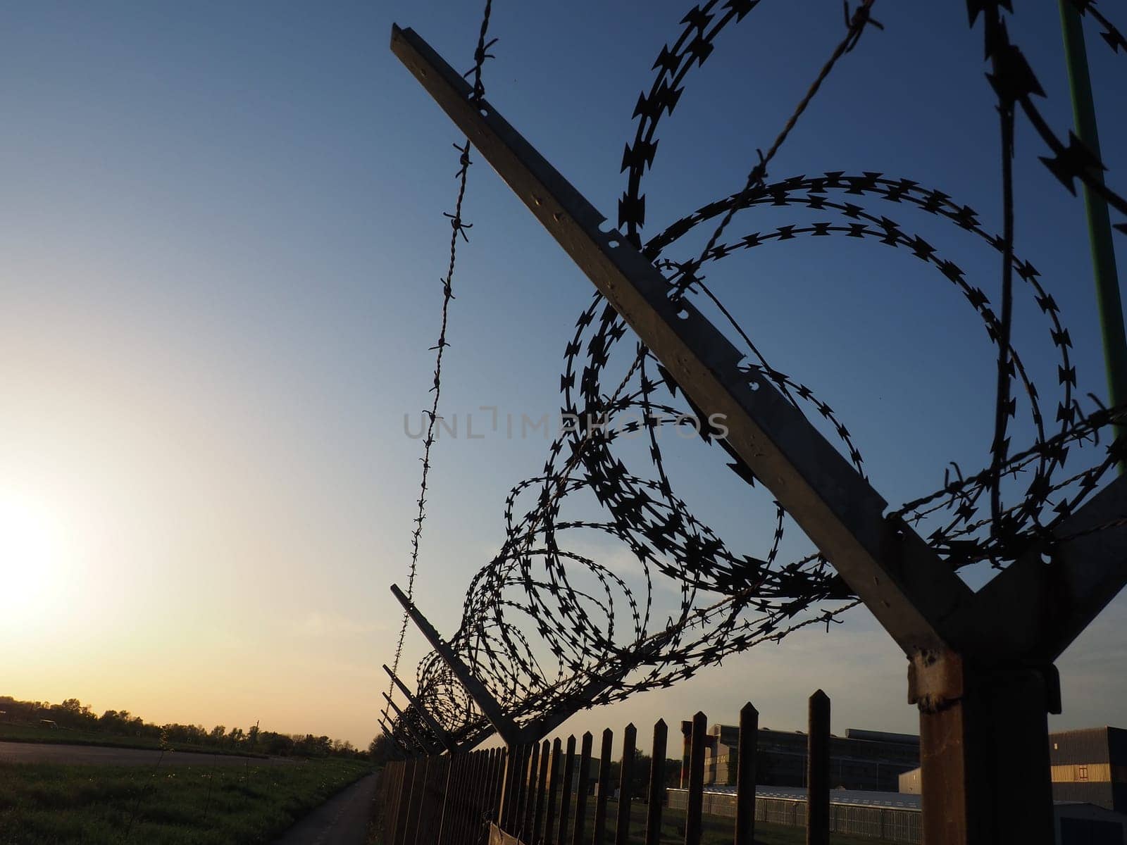 Barbed wire in skeins and stretched against the blue sky. Barbed wire against thieves and vandals. An insurmountable obstacle. Rusty wire, rows, spiral and coils of barbed wire